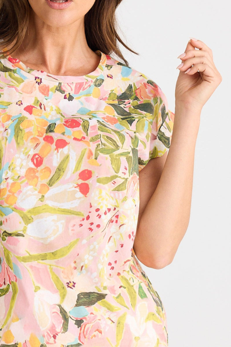 Woman wearing a colorful floral top and white shorts on a light gray background