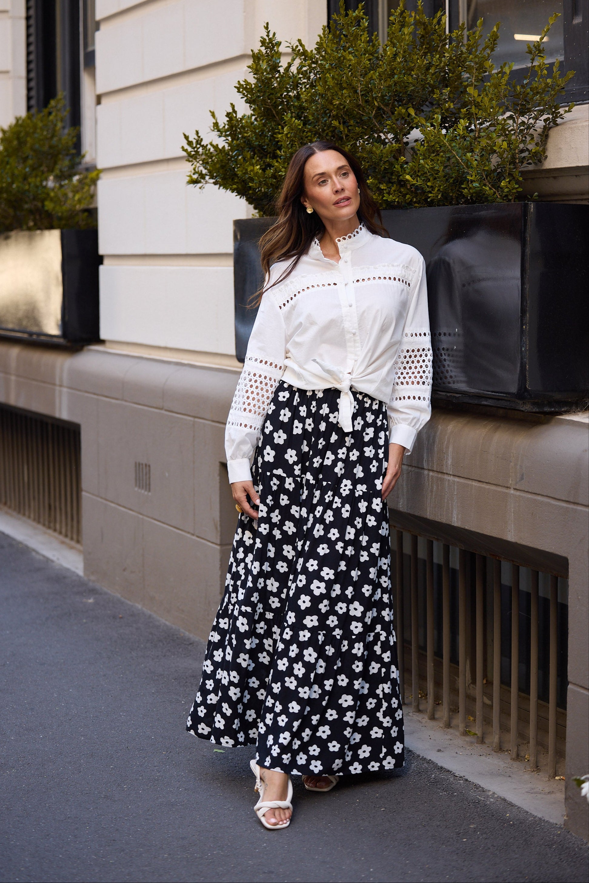 Woman in a white blouse and black floral skirt standing on a street.