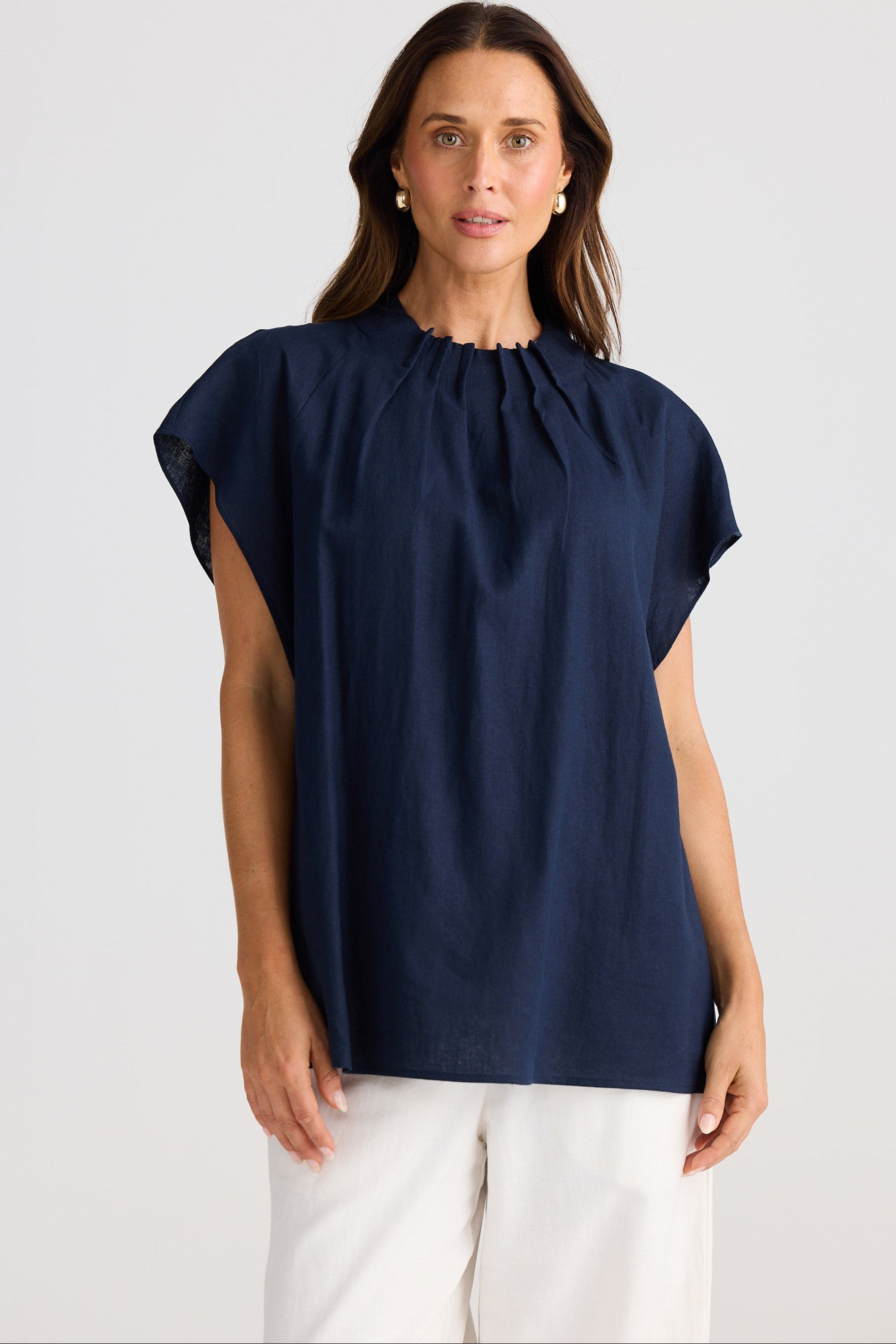 Woman wearing a navy blue blouse with white pants on a light gray background