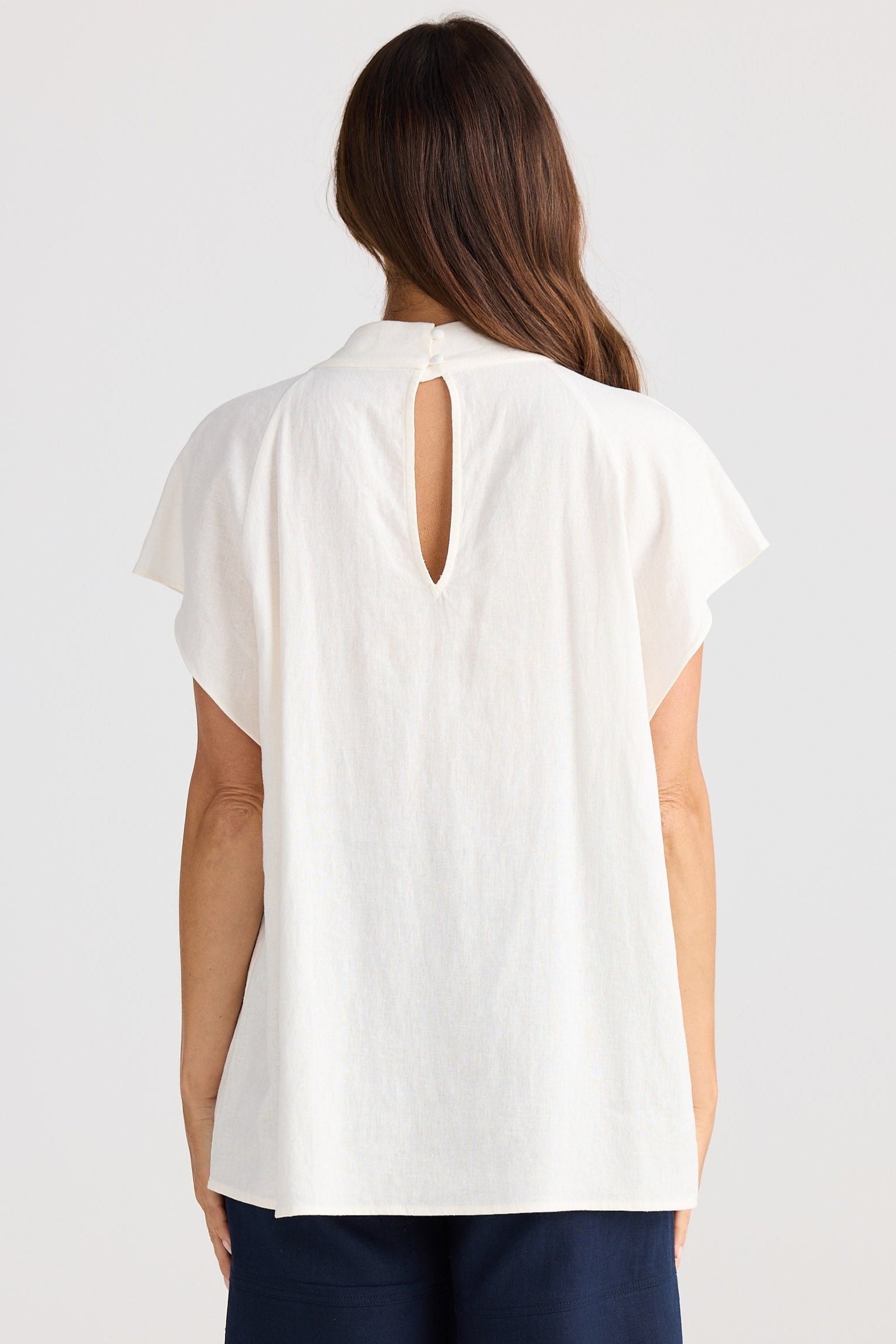 Woman wearing a white top with a cutout back design and navy shorts on a white background