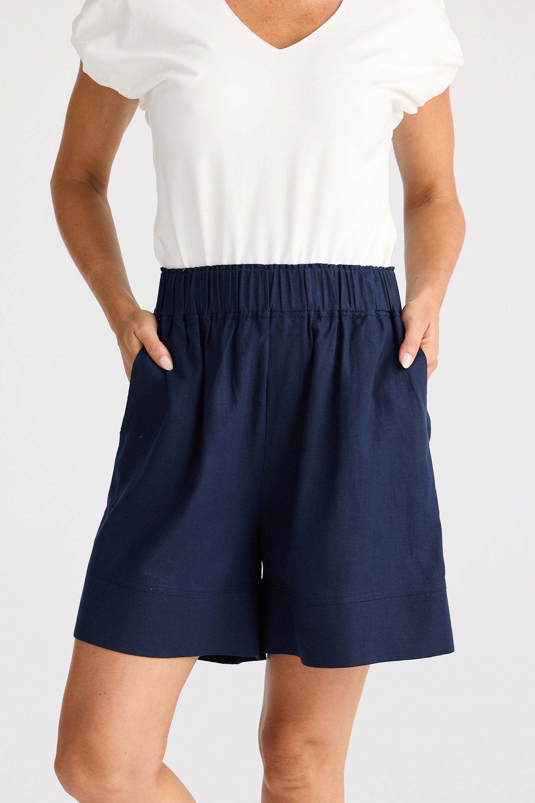 Person wearing navy shorts and a white top on a plain background