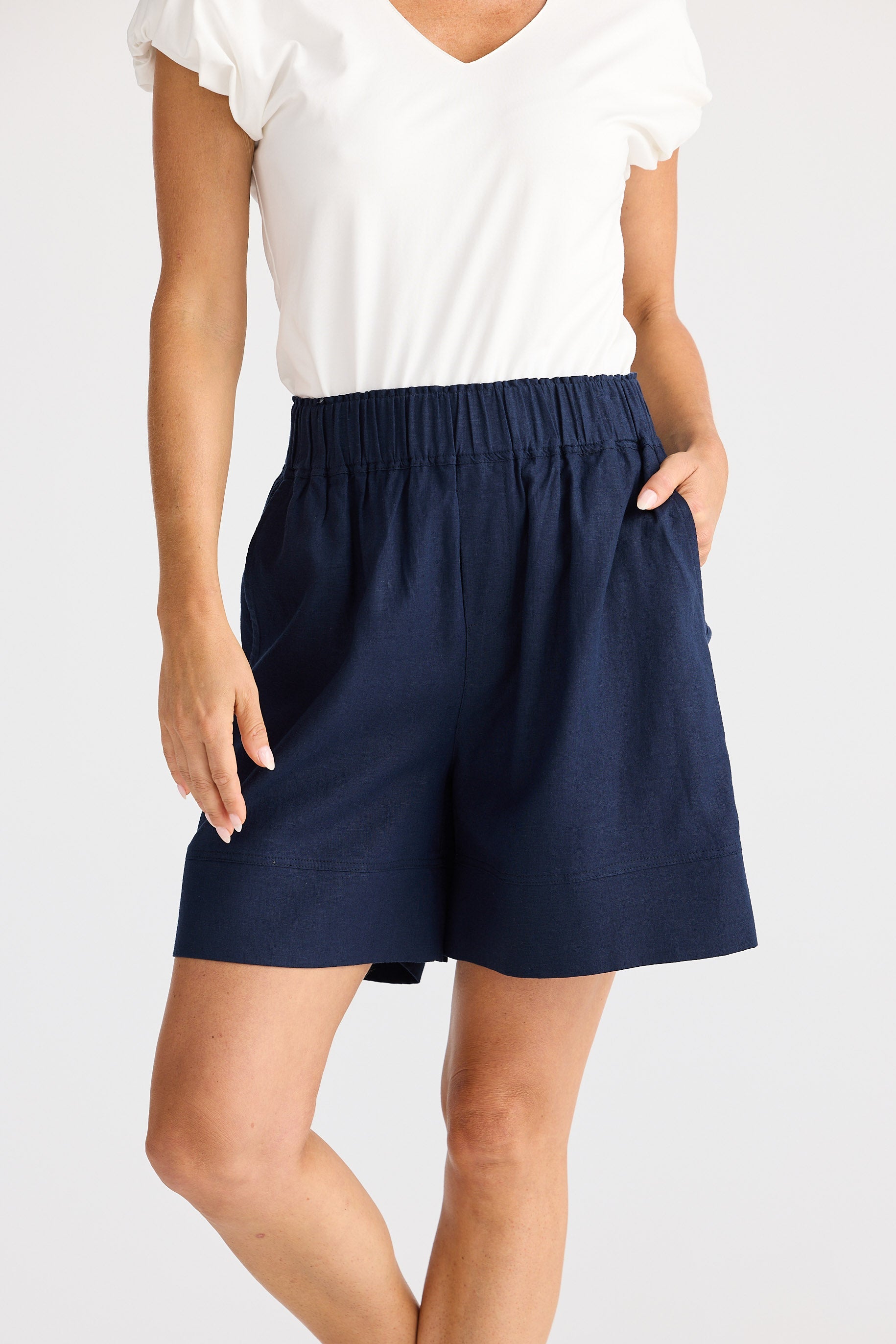 Person wearing navy shorts and a white top on a plain background