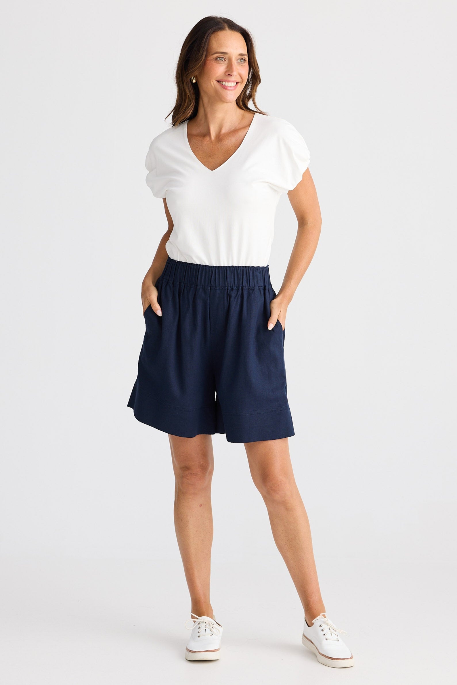 Woman wearing a white top and navy shorts on a white background