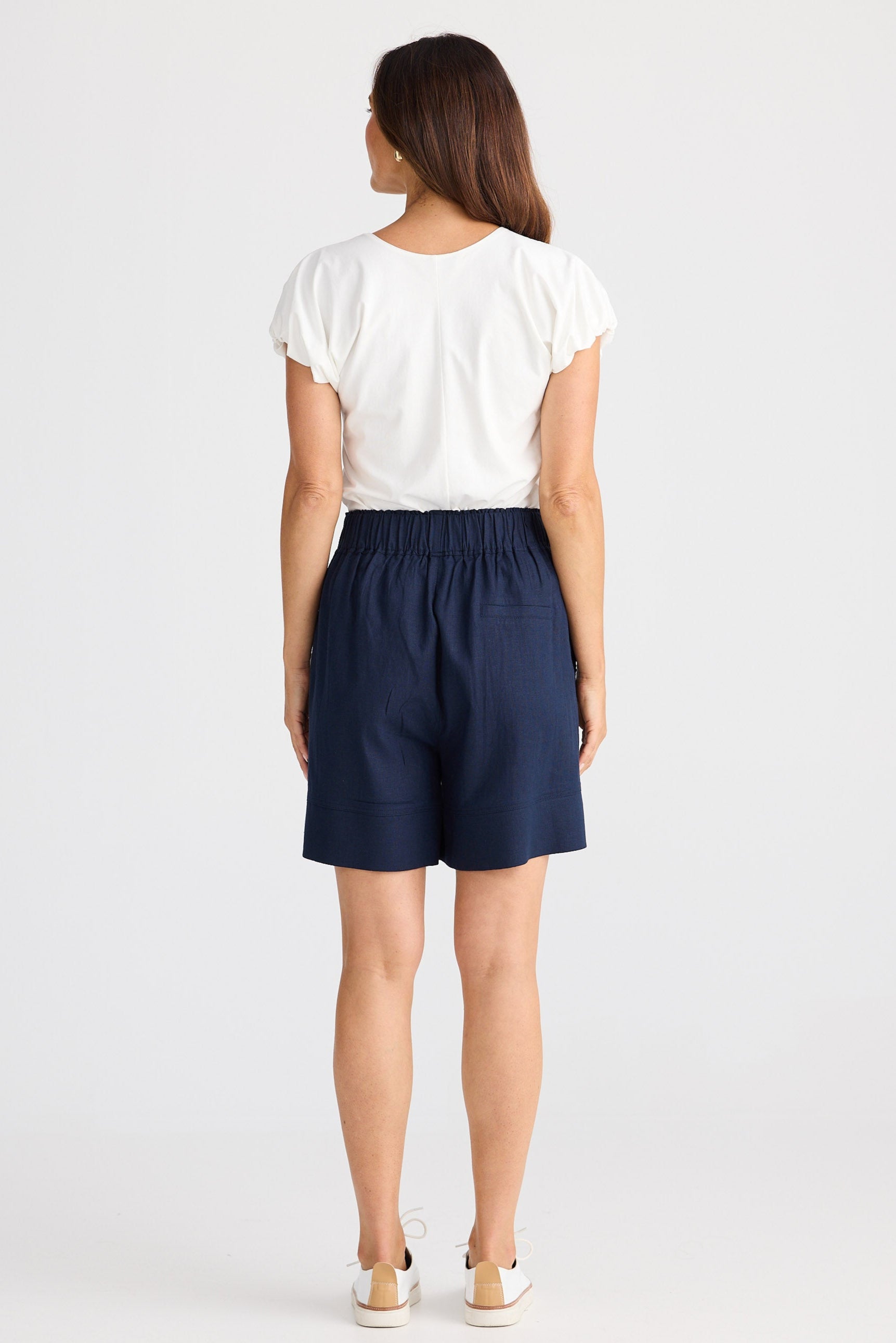Woman wearing navy shorts and a white top on a white background