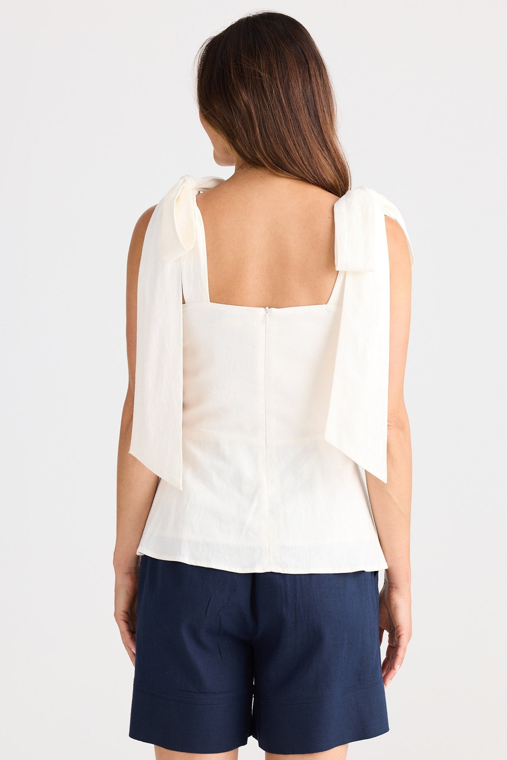 Woman wearing a white sleeveless top and navy shorts on a white background