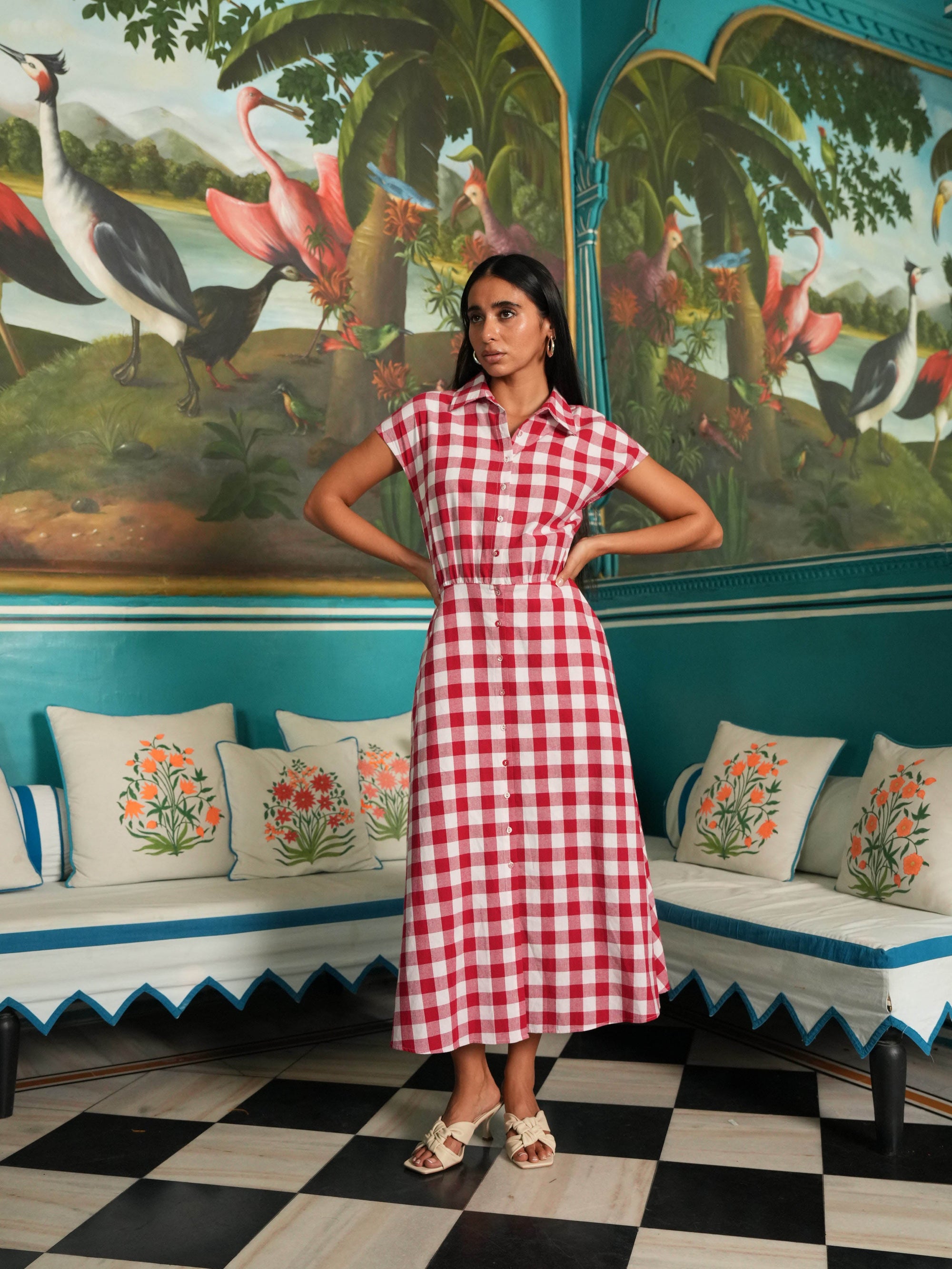 Woman in a red and white checkered dress standing in a room with decorative walls and furniture.