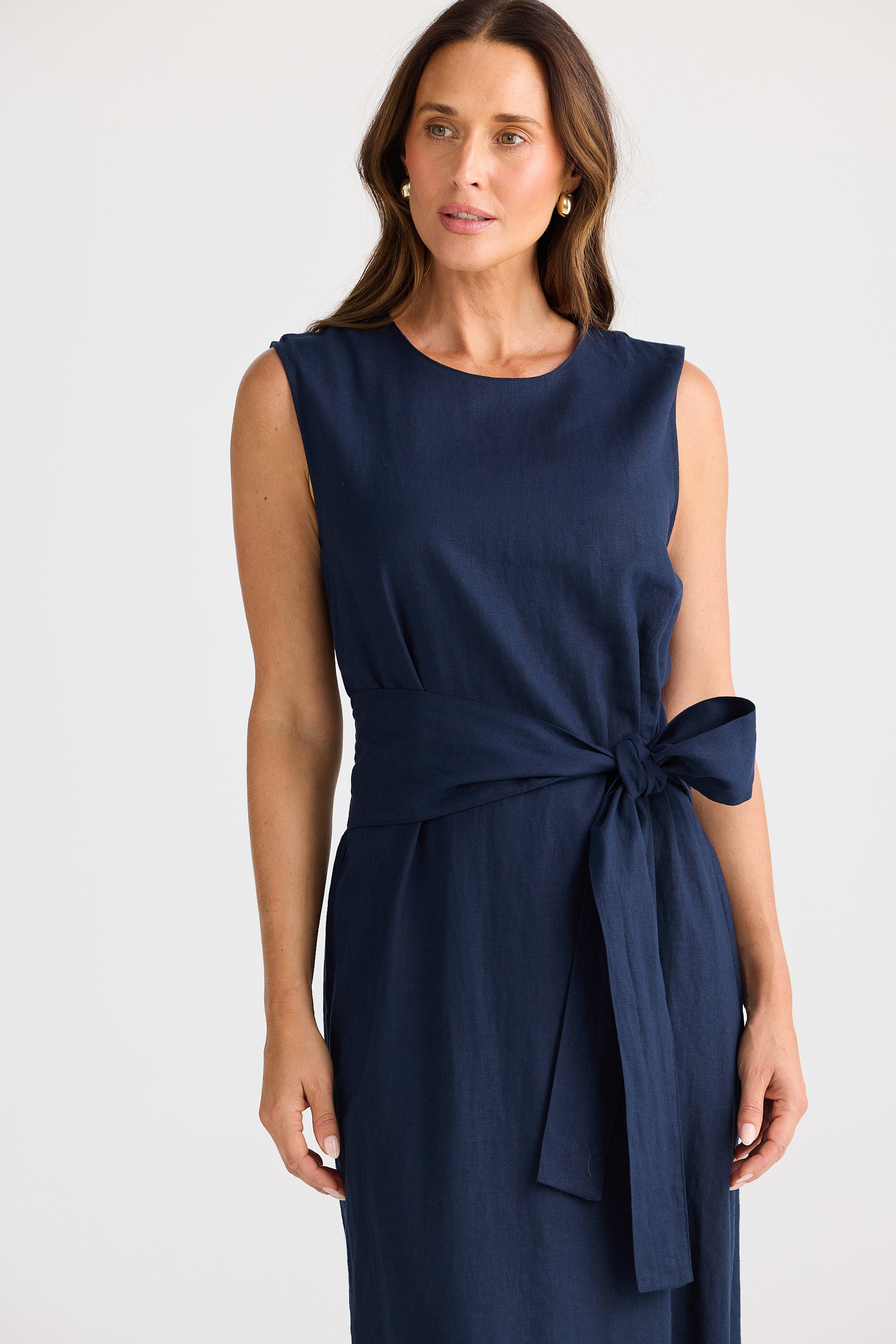 Woman wearing a navy blue sleeveless dress with a bow detail on a white background