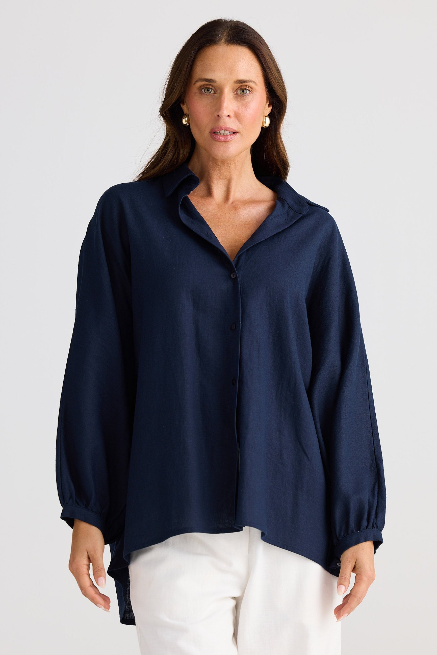 Woman wearing a navy blue blouse and white pants on a light gray background