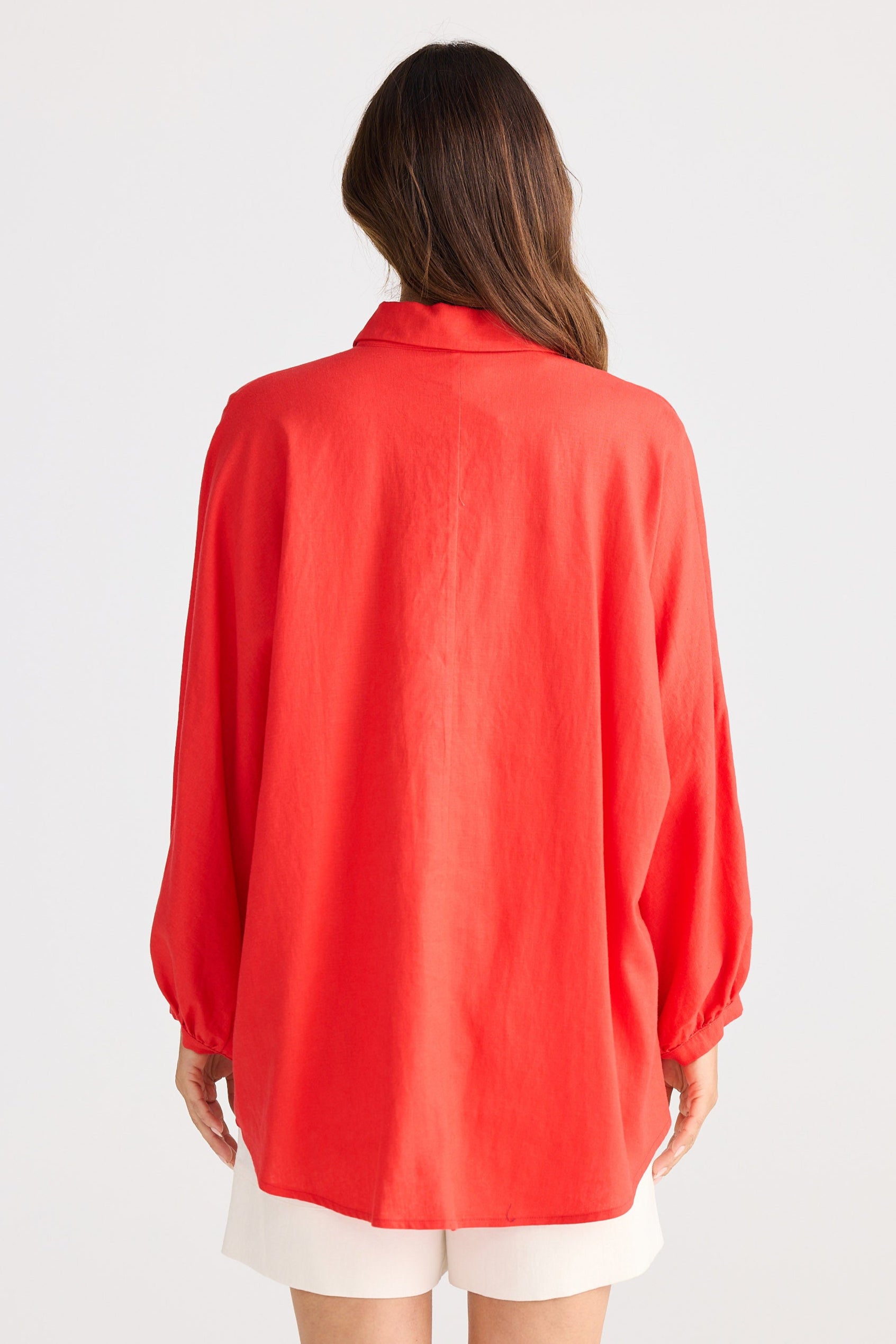 Person wearing a red shirt and white shorts on a plain background
