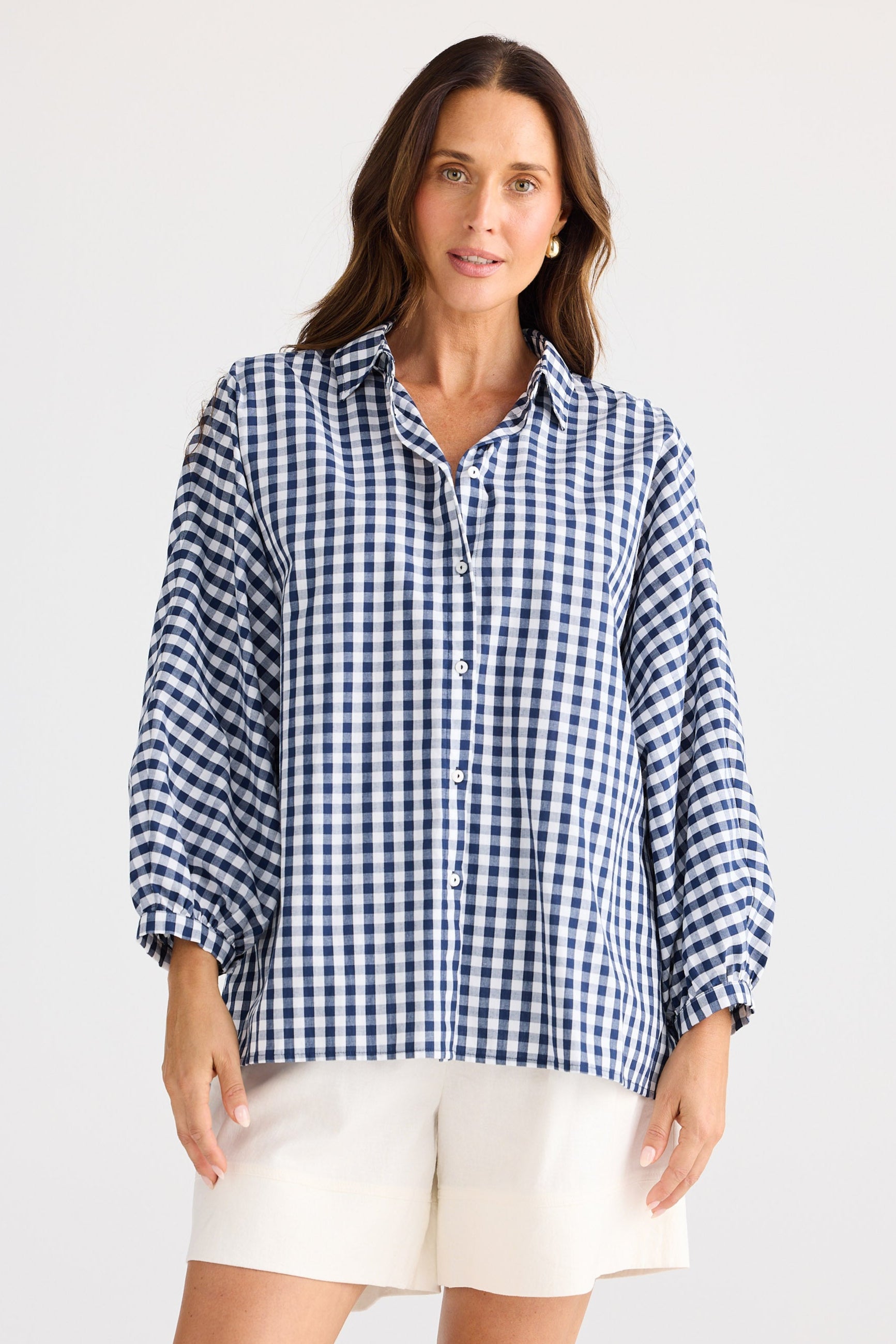 Woman wearing a blue and white checkered shirt with white shorts on a plain background