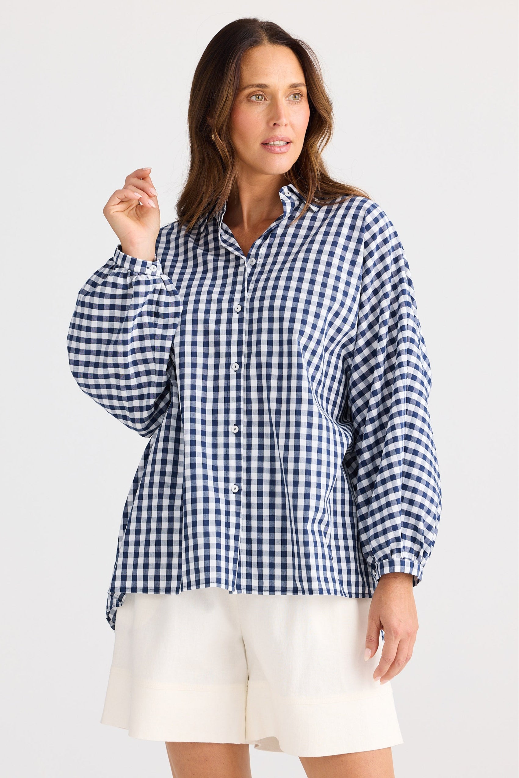 Woman wearing a blue and white checkered shirt with white shorts on a light gray background
