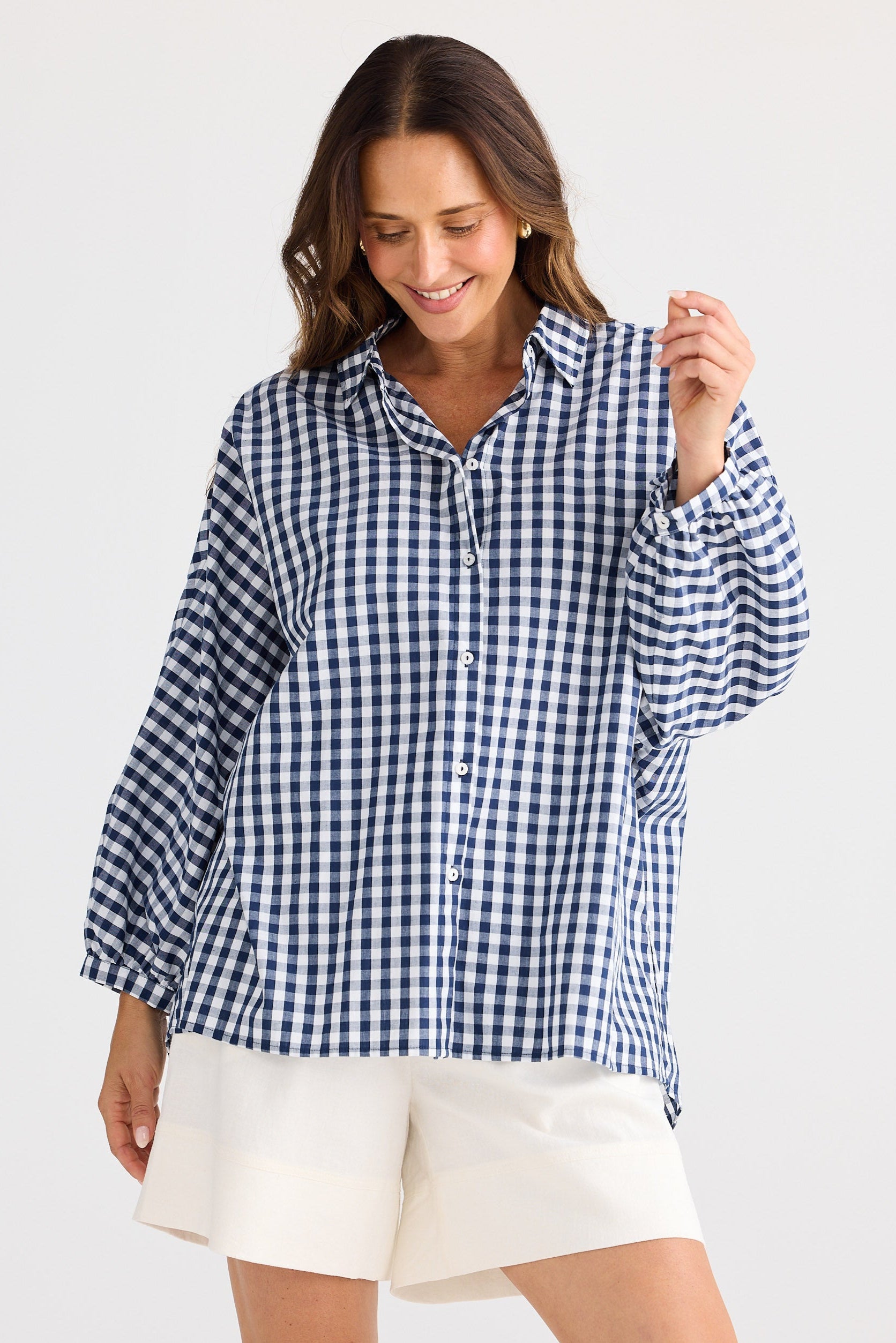 Woman wearing a blue and white checkered shirt and white shorts on a light gray background