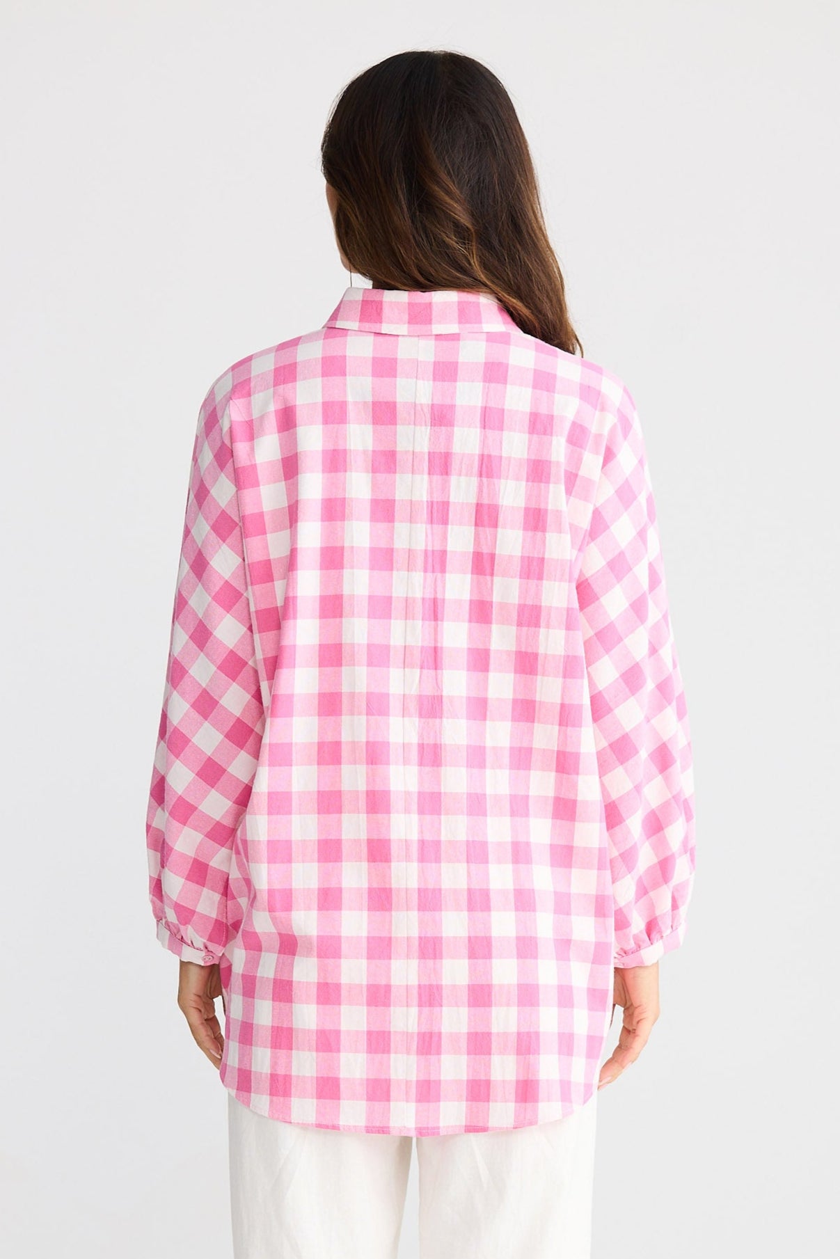 Person wearing a pink and white checkered shirt with white pants on a light gray background