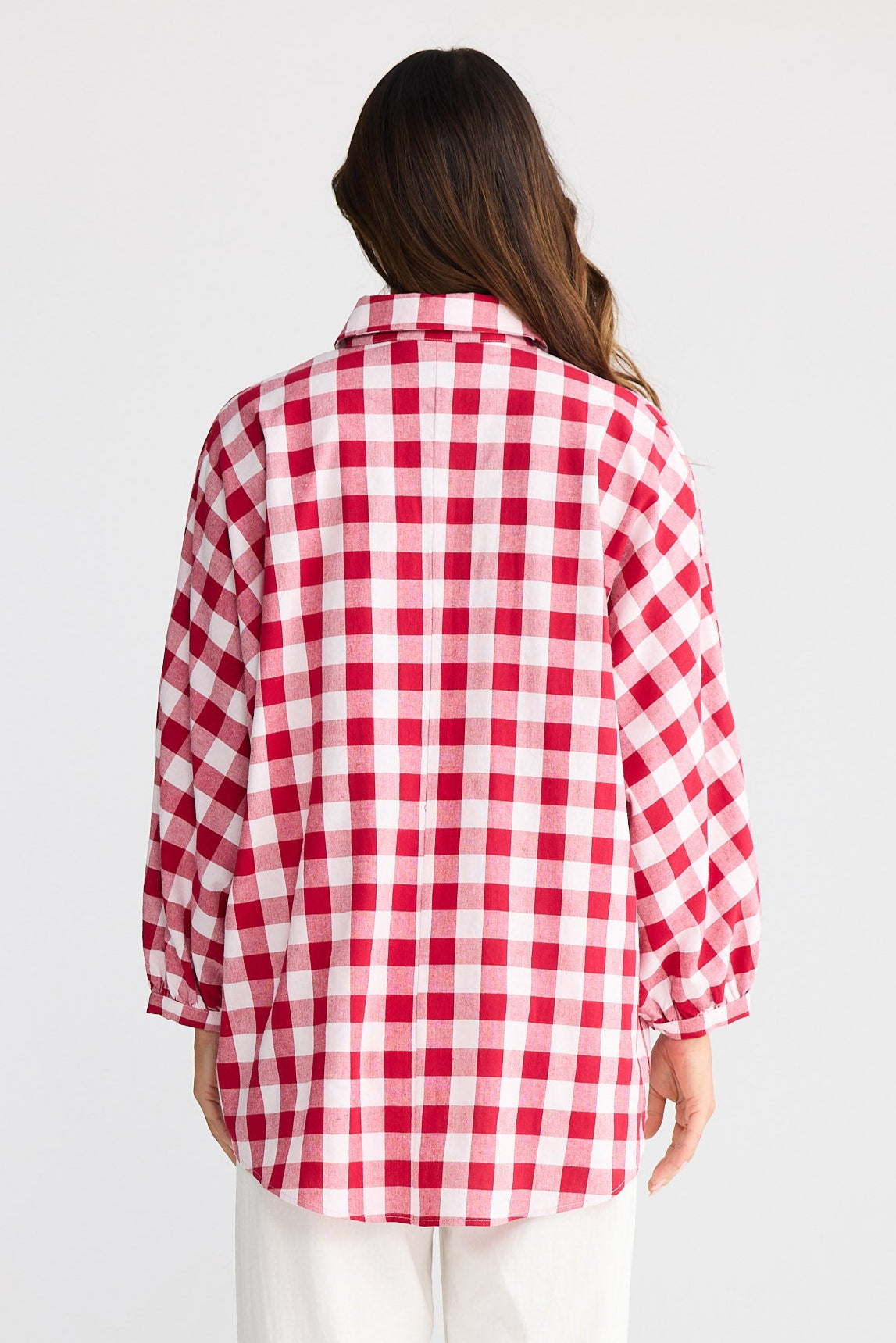 Person wearing a red and white checkered shirt and white pants on a plain background