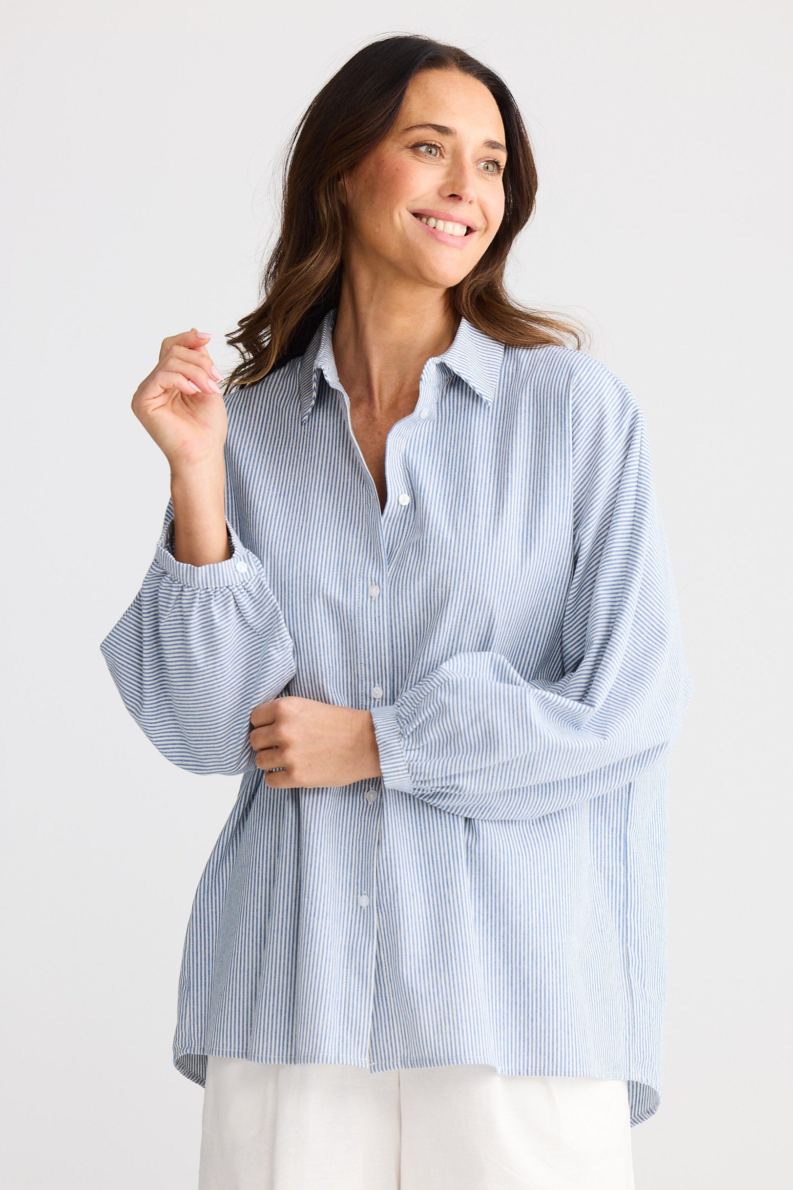 Woman wearing a light blue striped shirt and white shorts on a plain background
