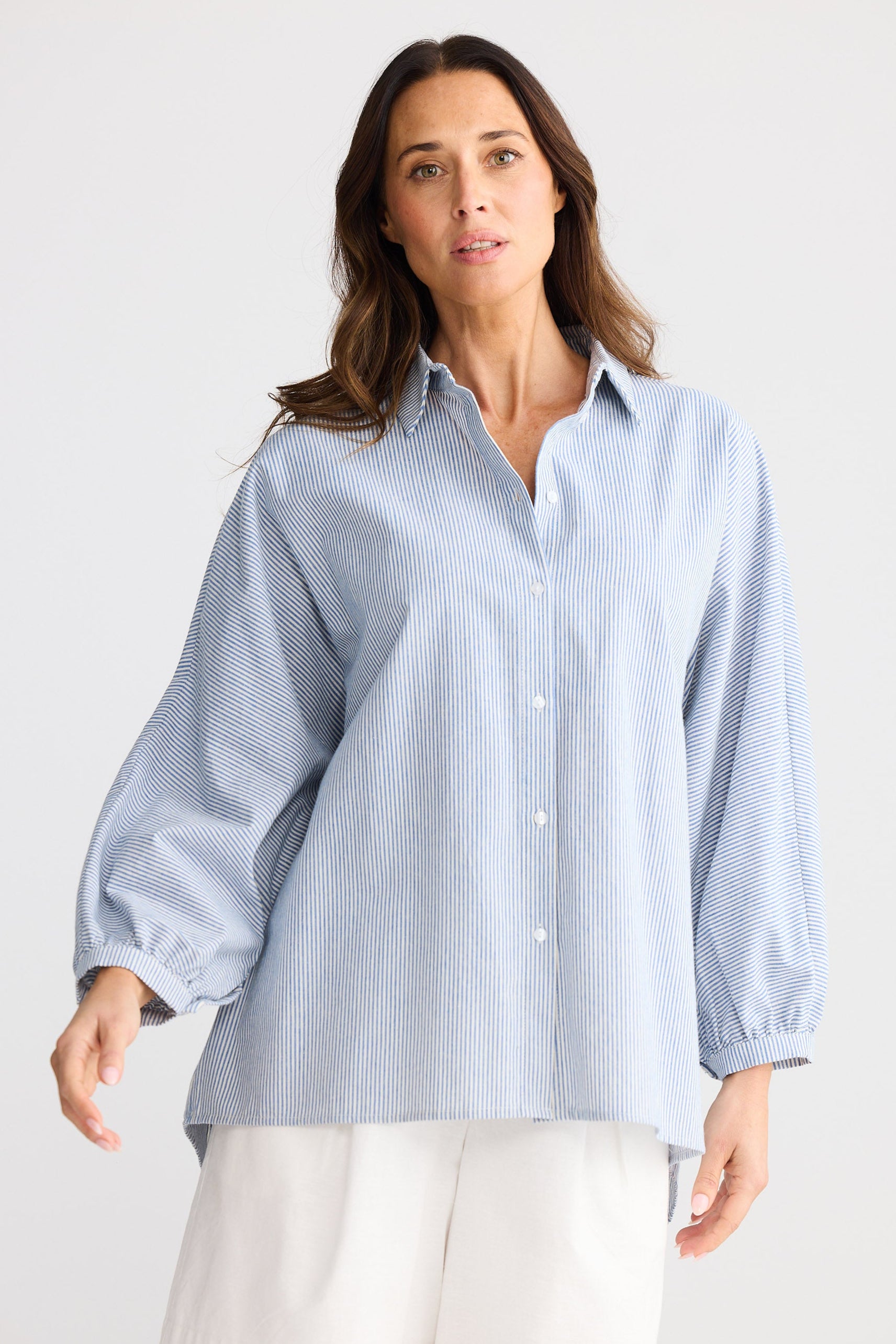 Woman wearing a light blue striped shirt and white shorts on a plain background