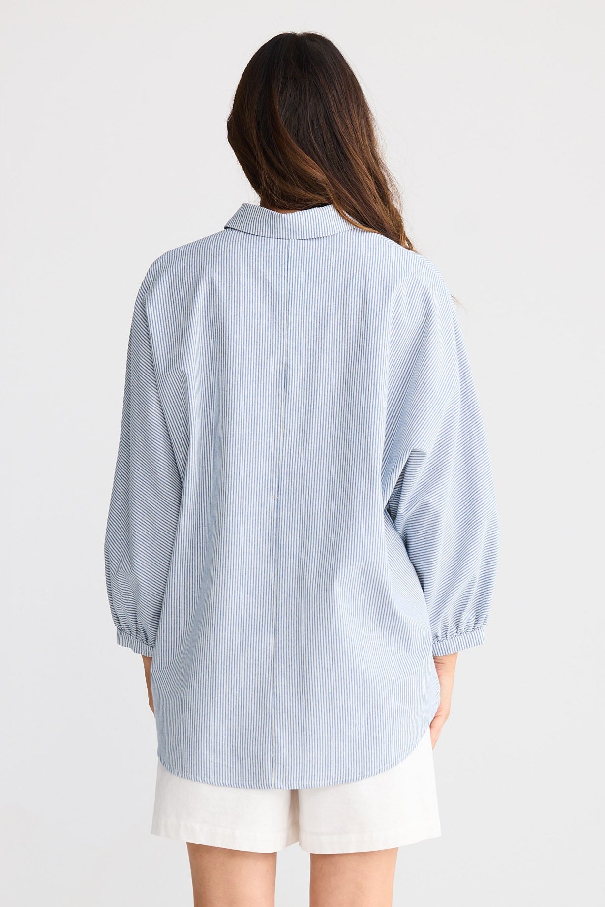 Person wearing a light blue striped shirt and white shorts on a plain background