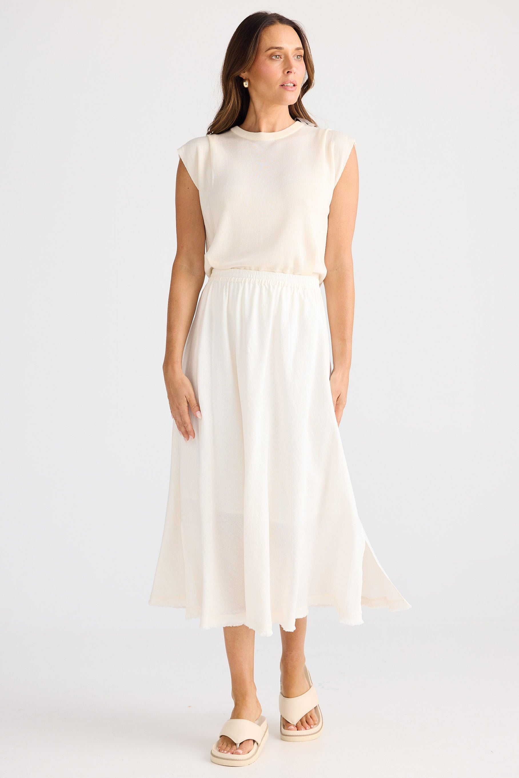 Woman wearing a white sleeveless top and skirt on a light gray background
