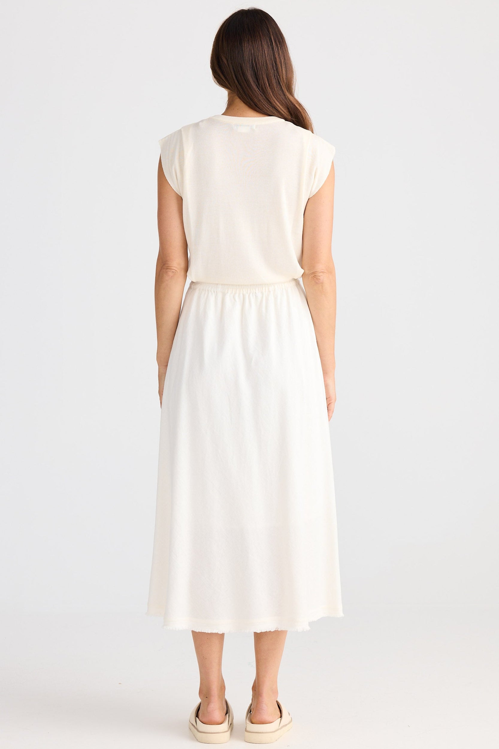 Woman wearing a white top and skirt on a plain background