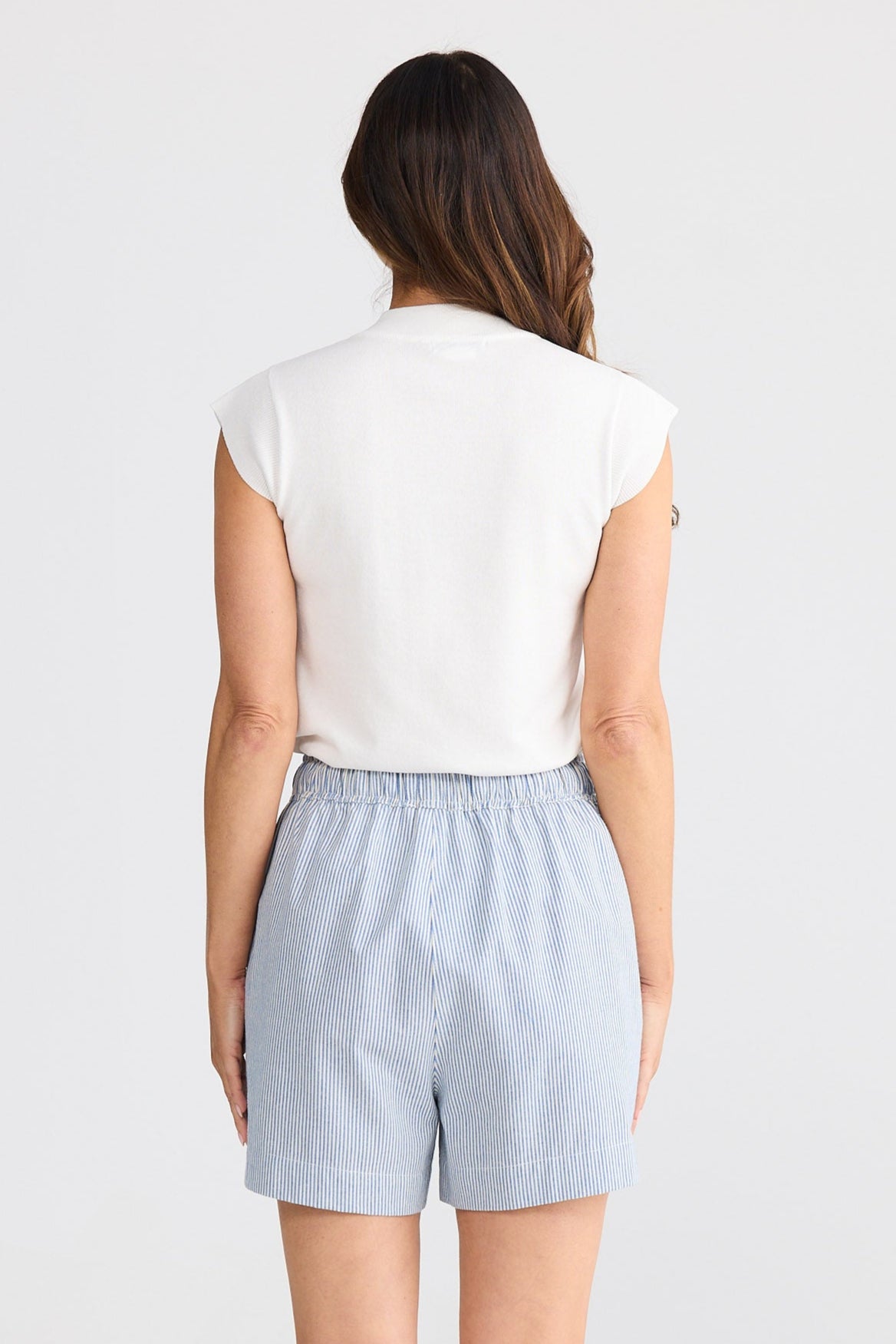 Woman wearing light blue shorts and a white top on a white background