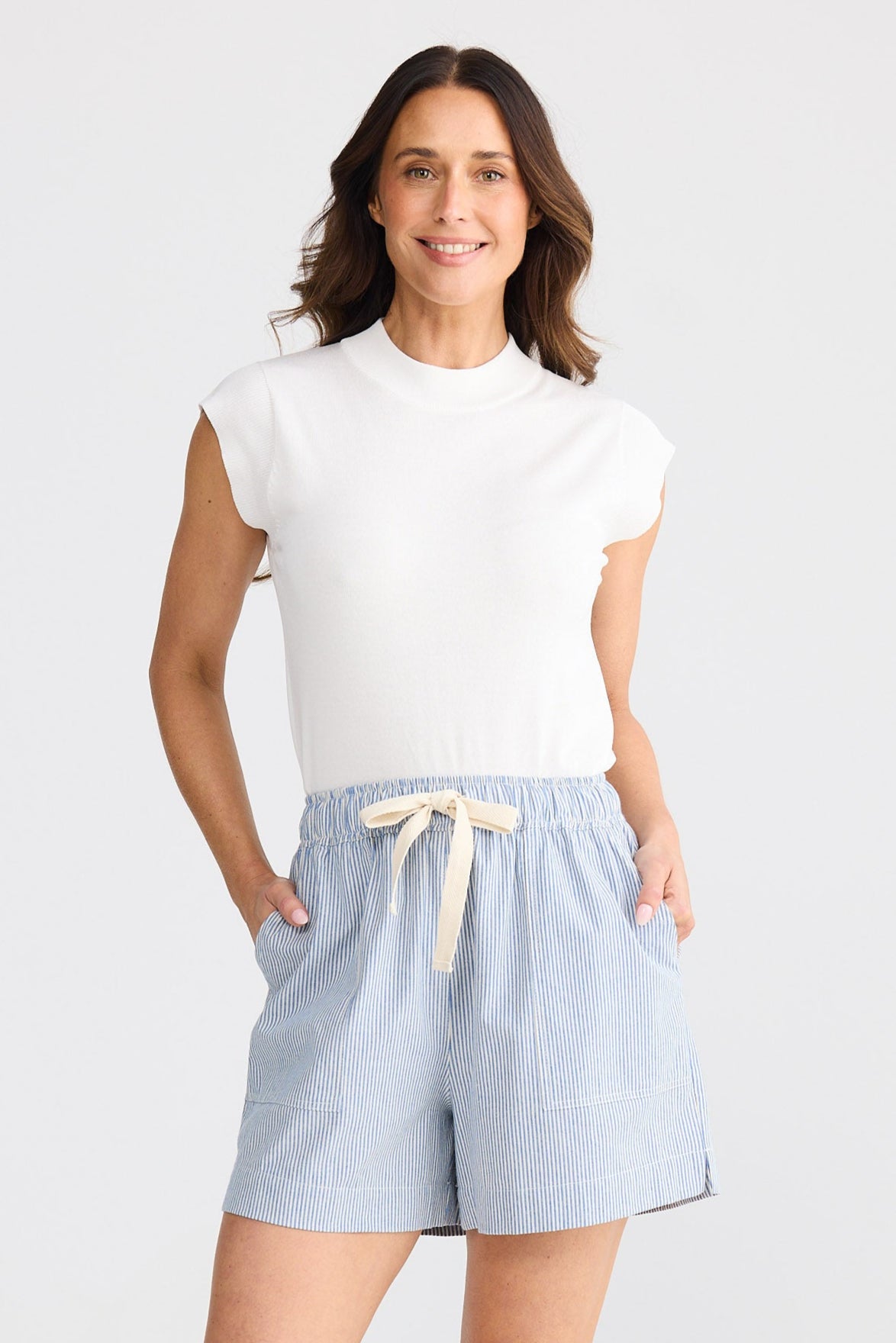 Woman wearing light blue shorts and a white top on a white background