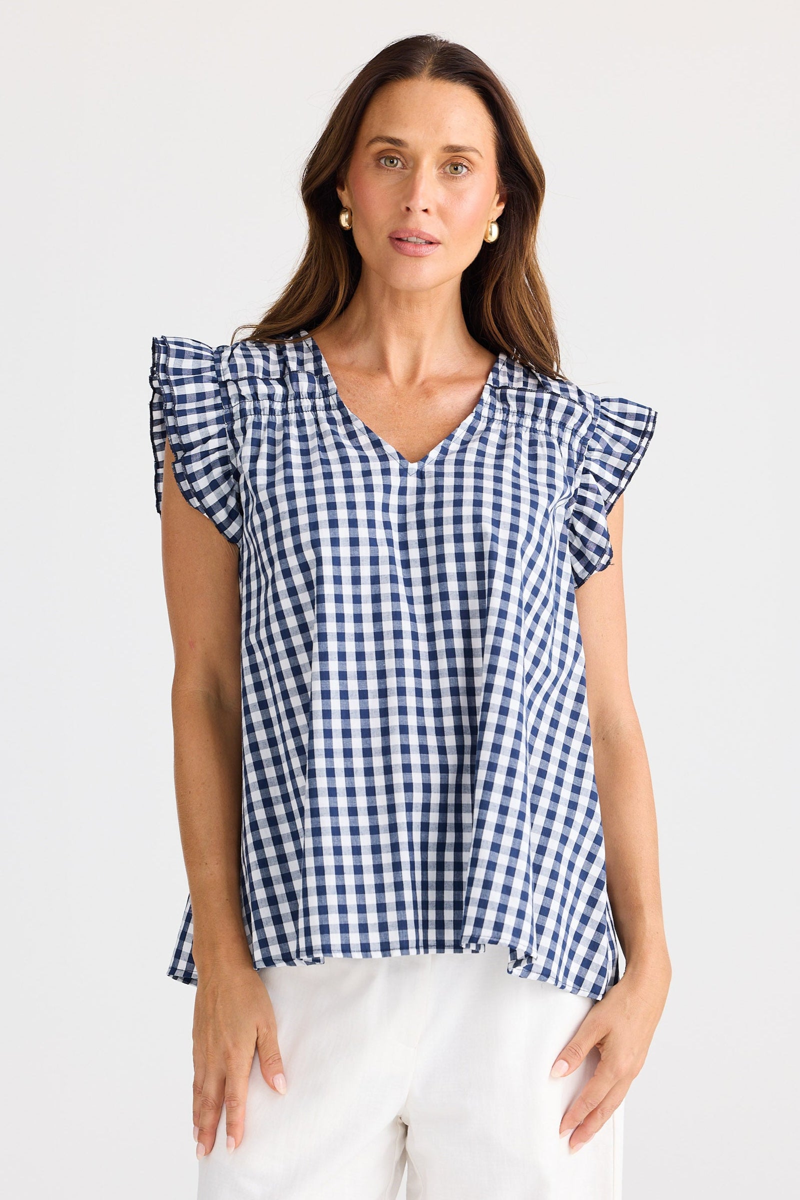 Woman wearing a blue and white checkered top with ruffled sleeves on a white background