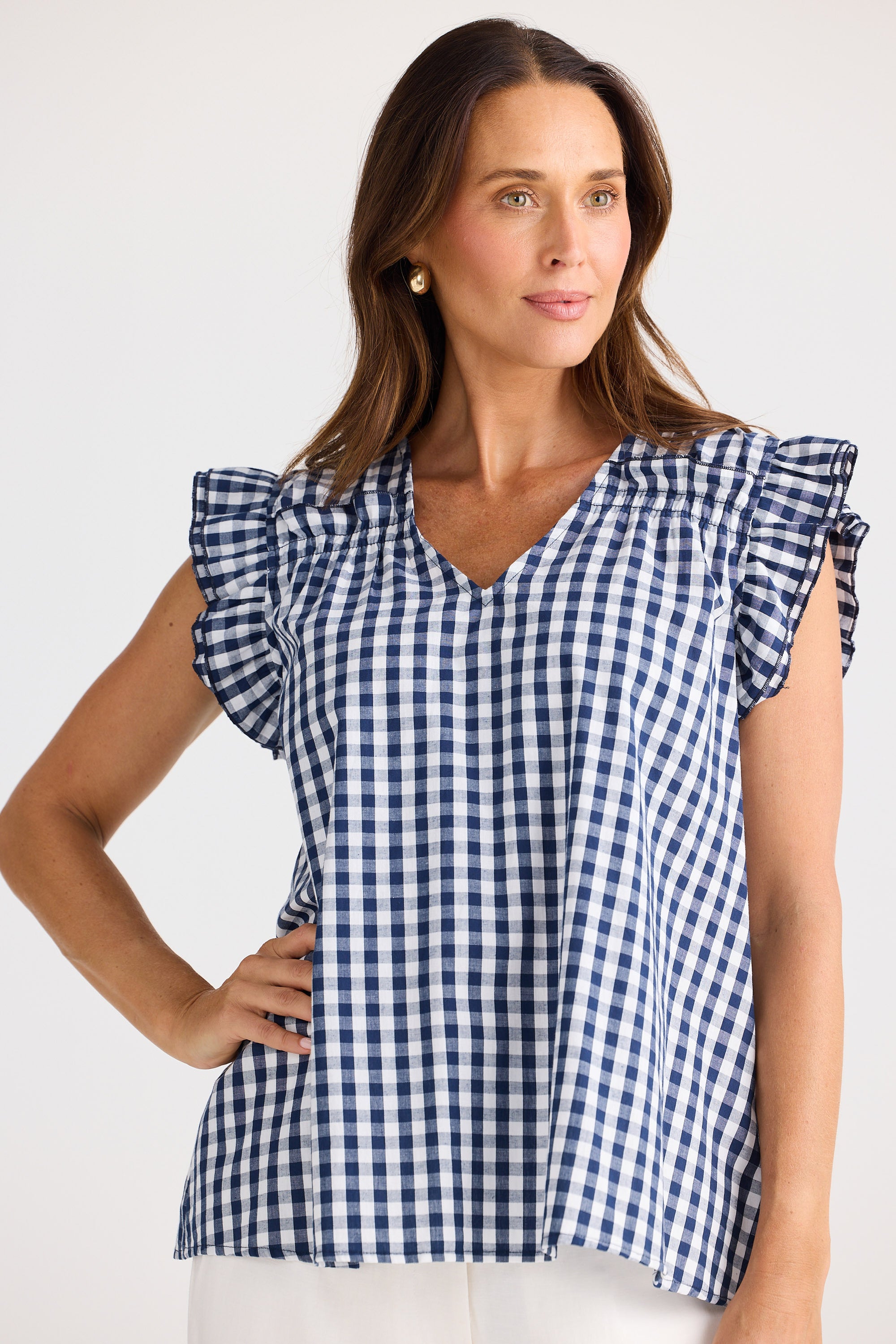 Woman wearing a blue and white checkered top with ruffled sleeves on a light background