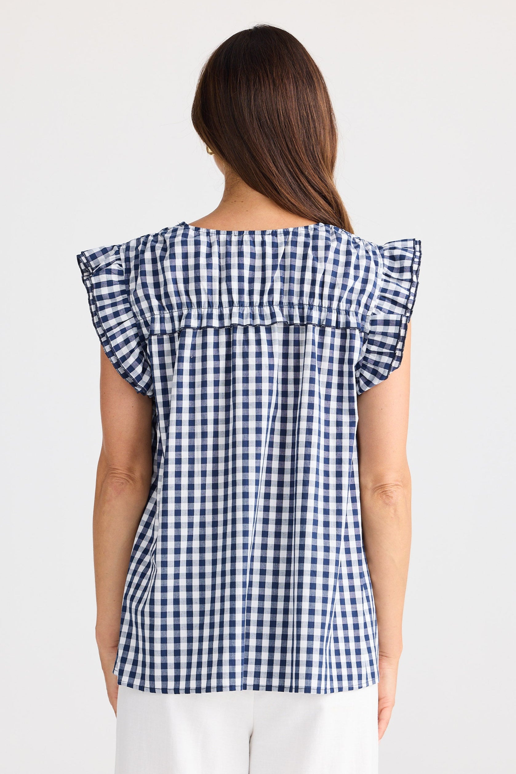 Woman wearing a blue and white checkered top with ruffled sleeves on a white background