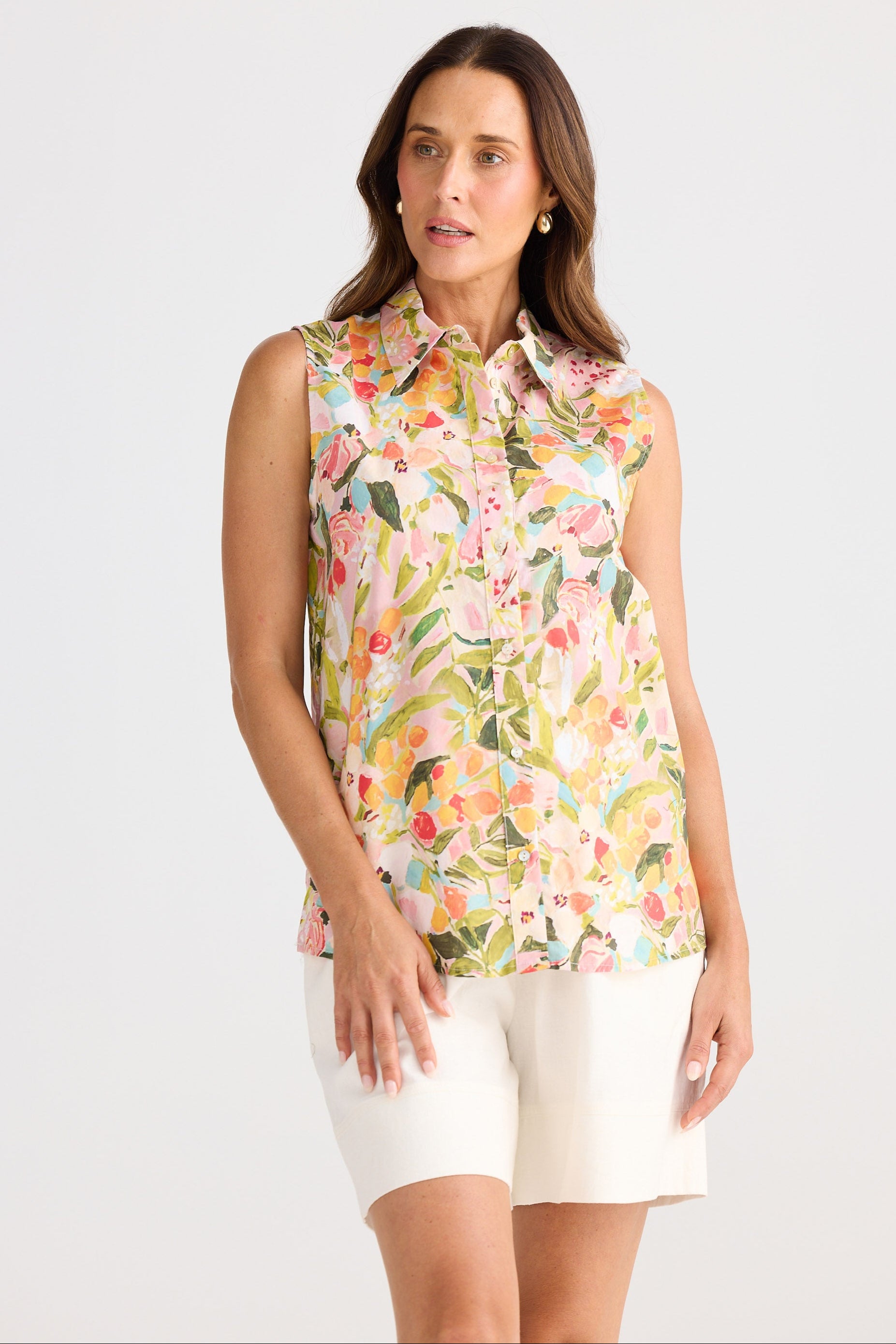 Woman wearing a sleeveless floral blouse and white shorts on a white background