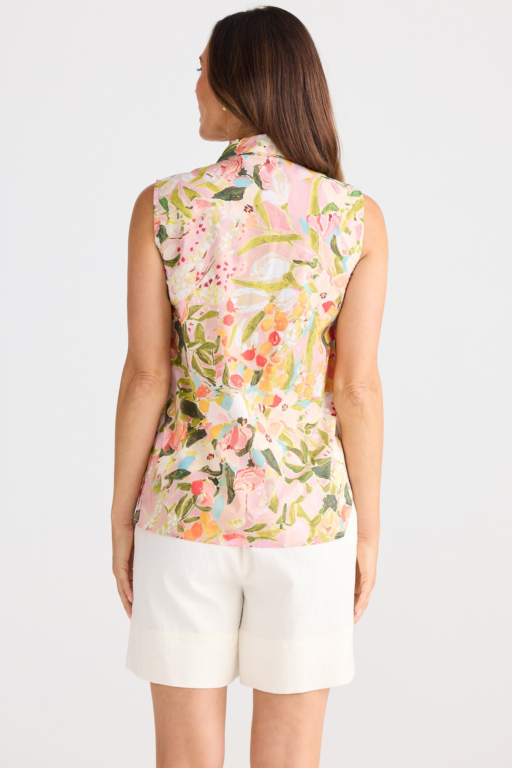 Woman wearing a sleeveless floral top and white shorts on a white background
