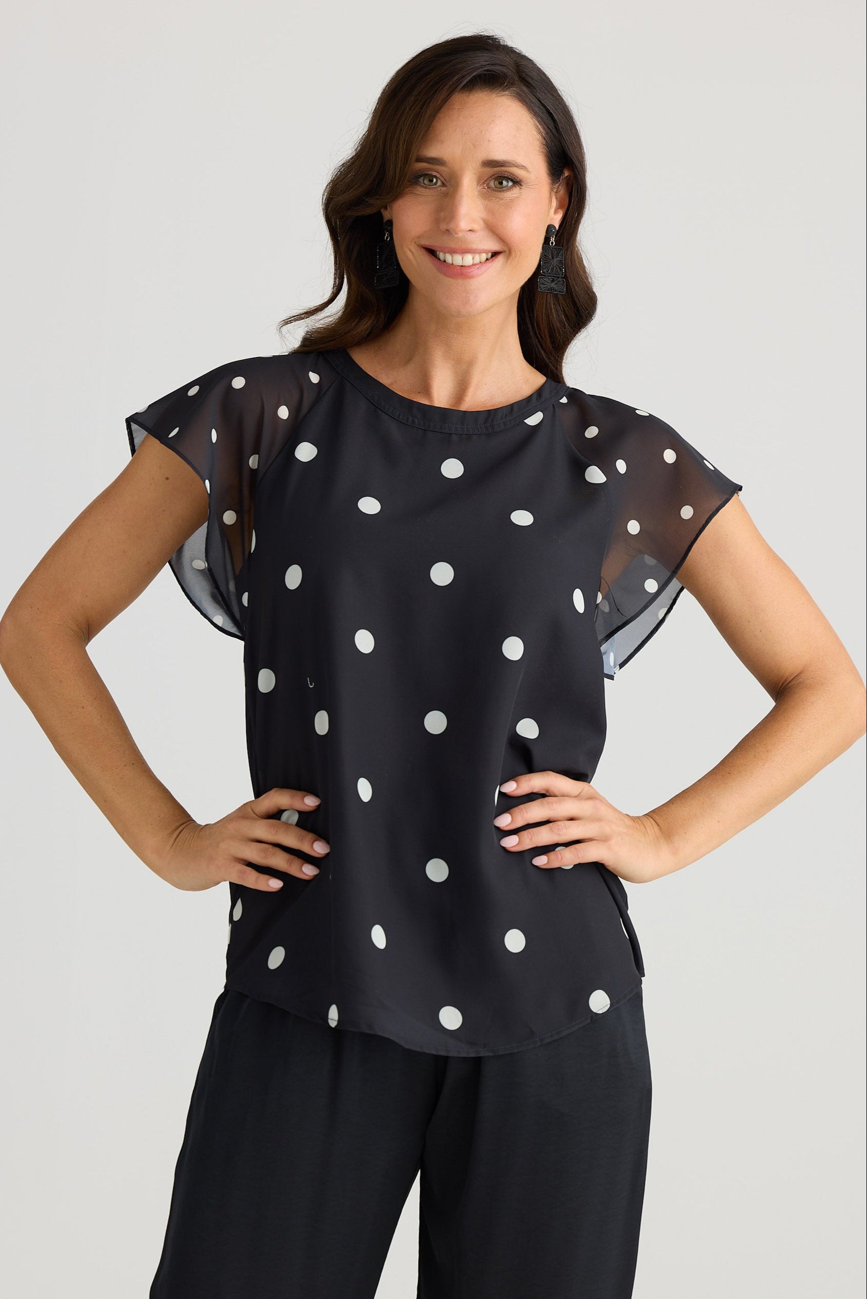 Woman wearing a black top with white polka dots and black pants on a light gray background