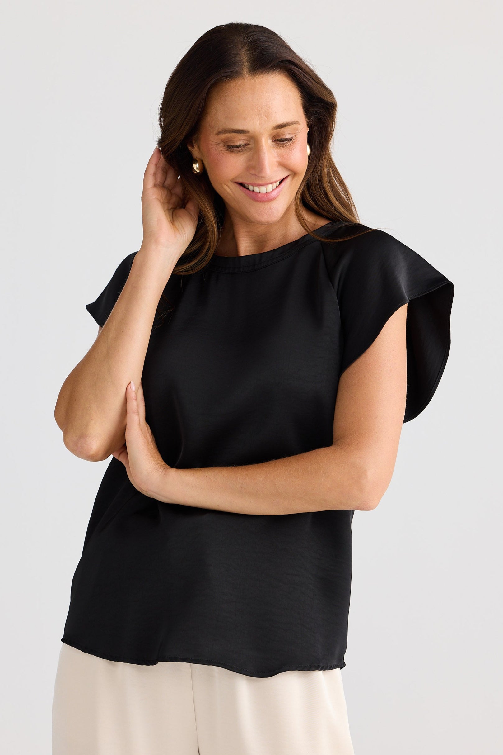 Woman wearing a black top and beige pants against a white background