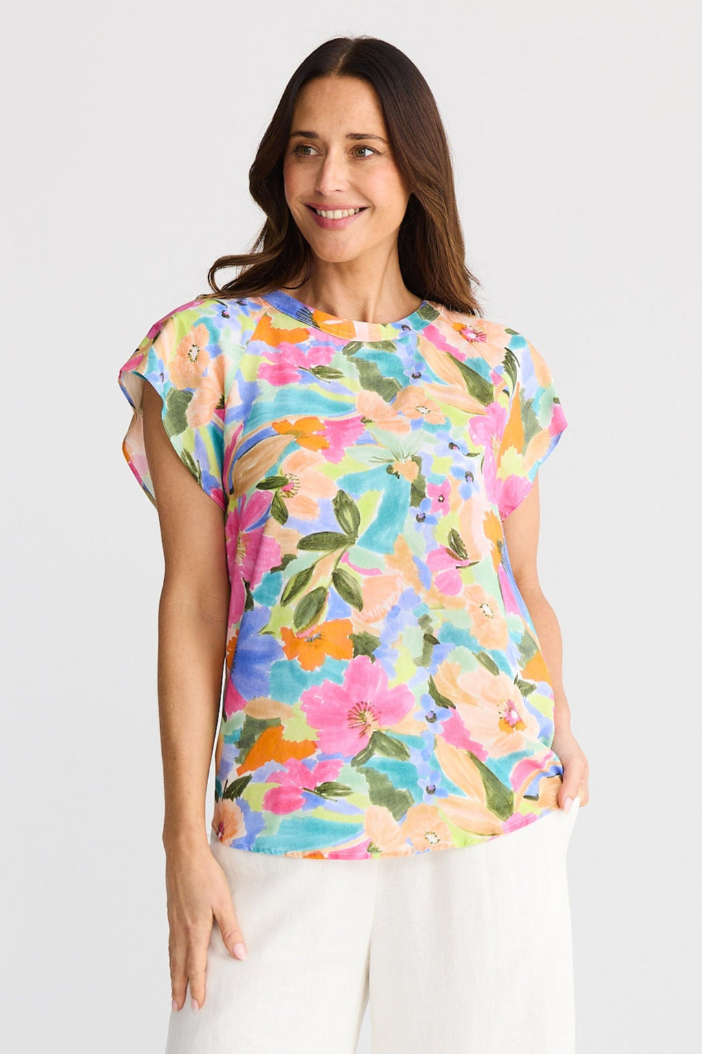 Woman wearing a colorful floral top and white pants on a white background