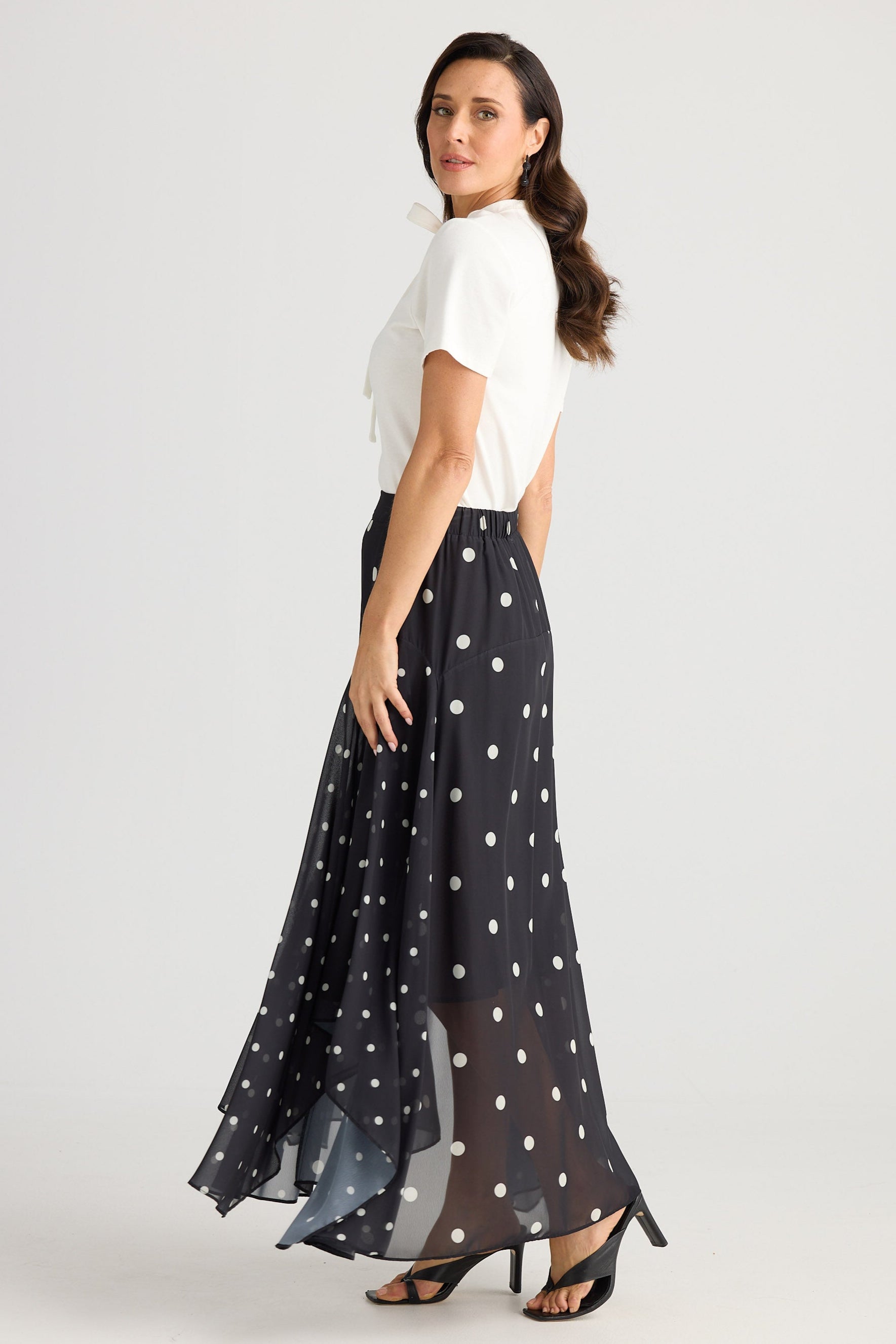 Woman wearing a white top and black polka dot skirt on a white background