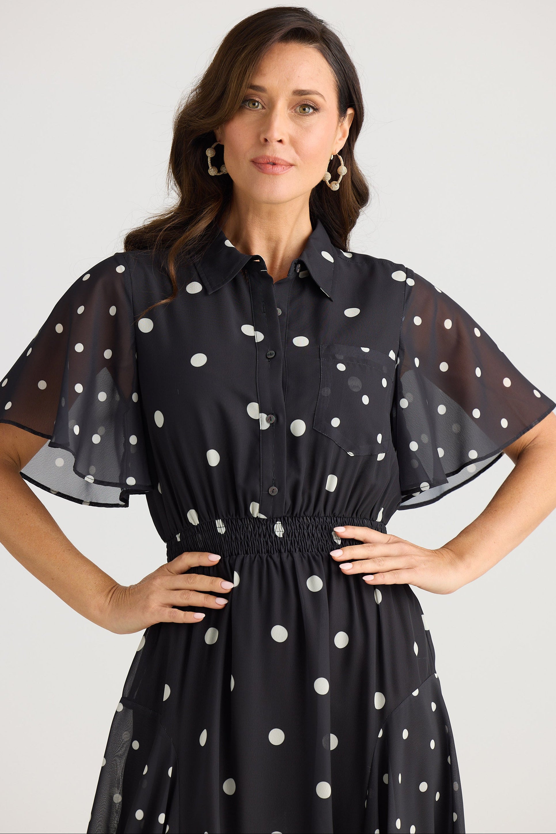 Woman wearing a black dress with white polka dots on a plain background