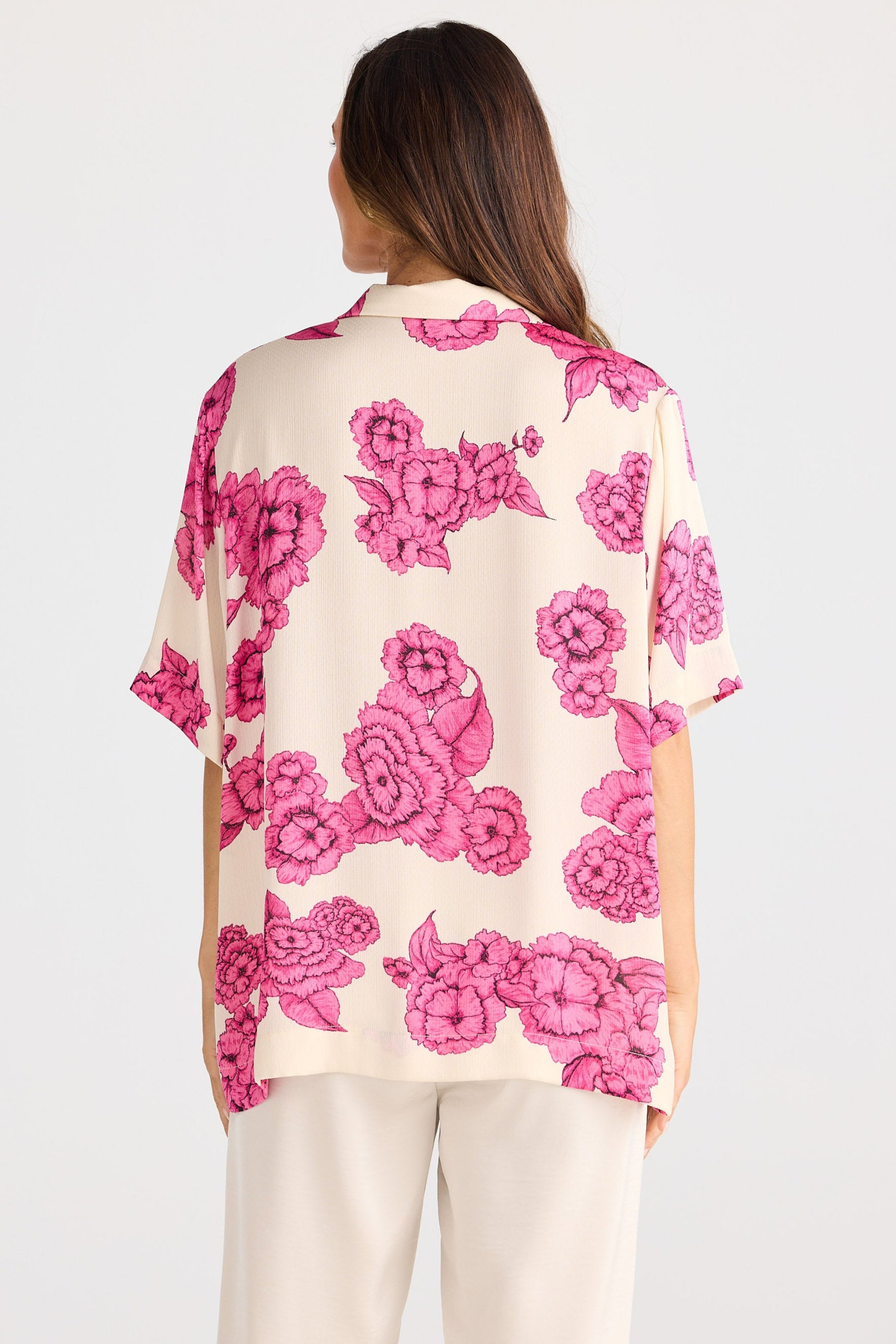 Woman wearing a floral shirt with pink flowers on a plain background