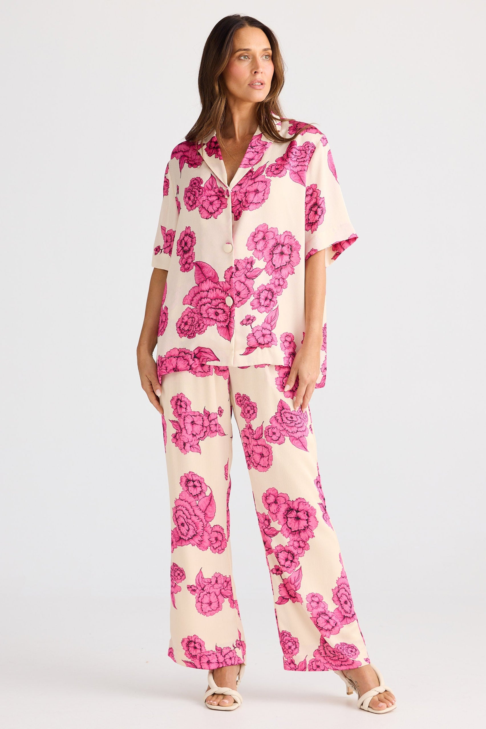 Woman wearing a pink floral shirt and pant set on a white background