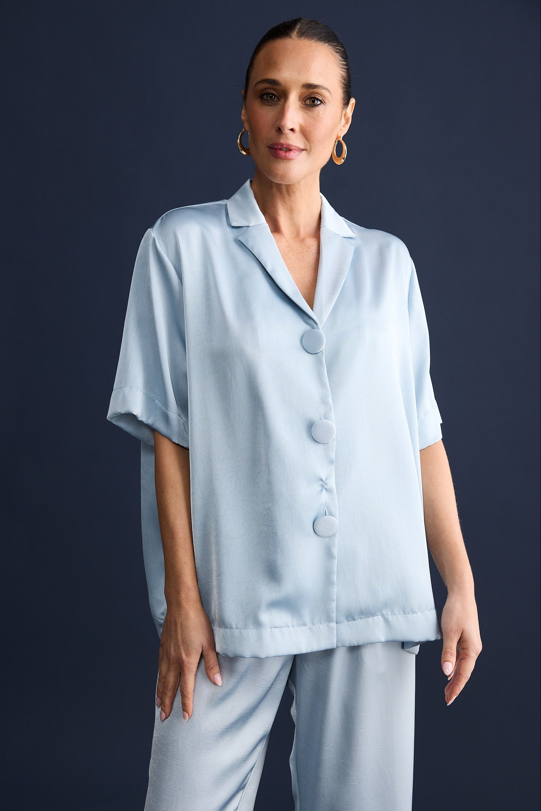 Woman wearing light blue silky set set against a dark background