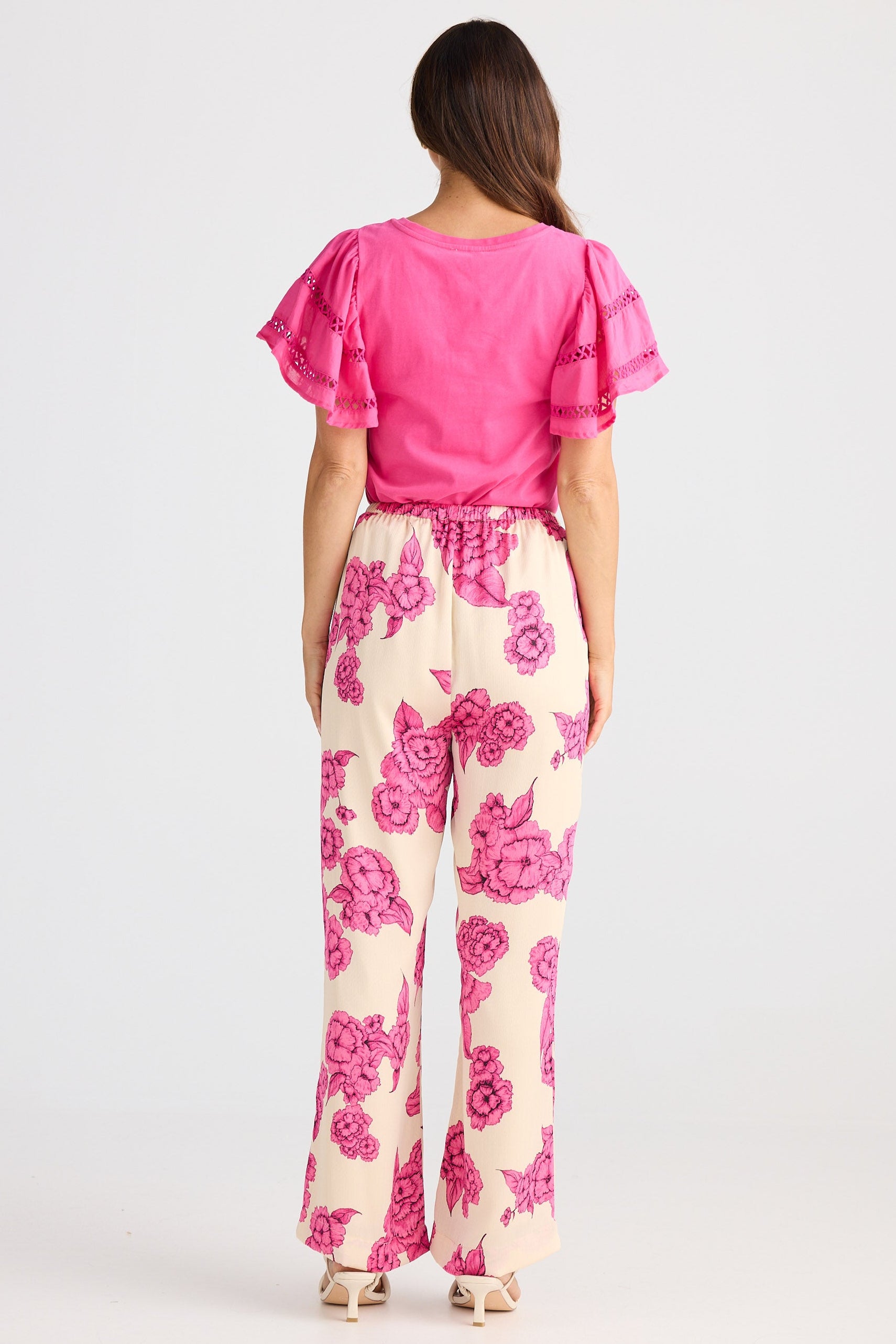 Woman wearing a pink top and floral pants on a white background
