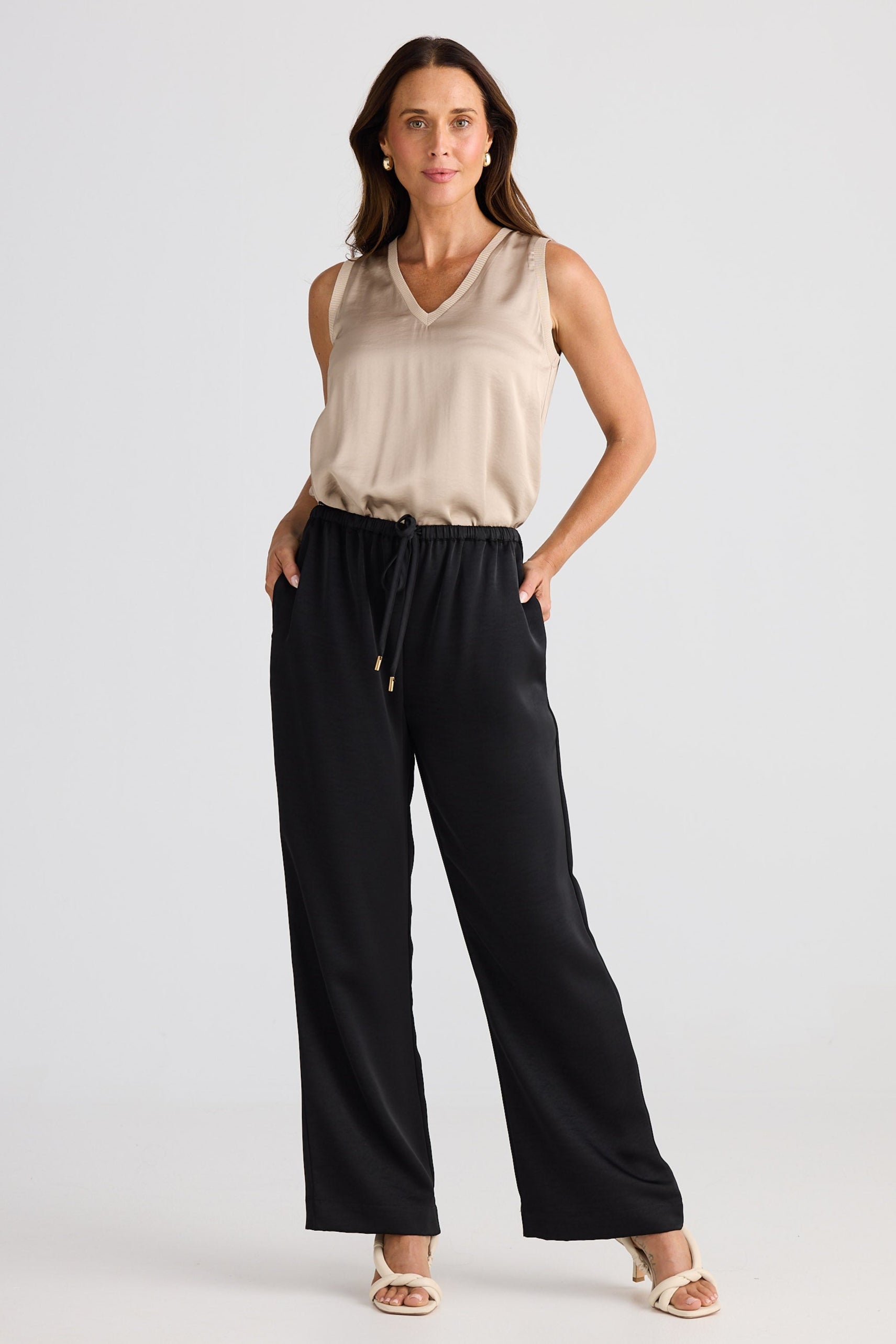 Woman wearing a beige sleeveless top and black pants on a white background