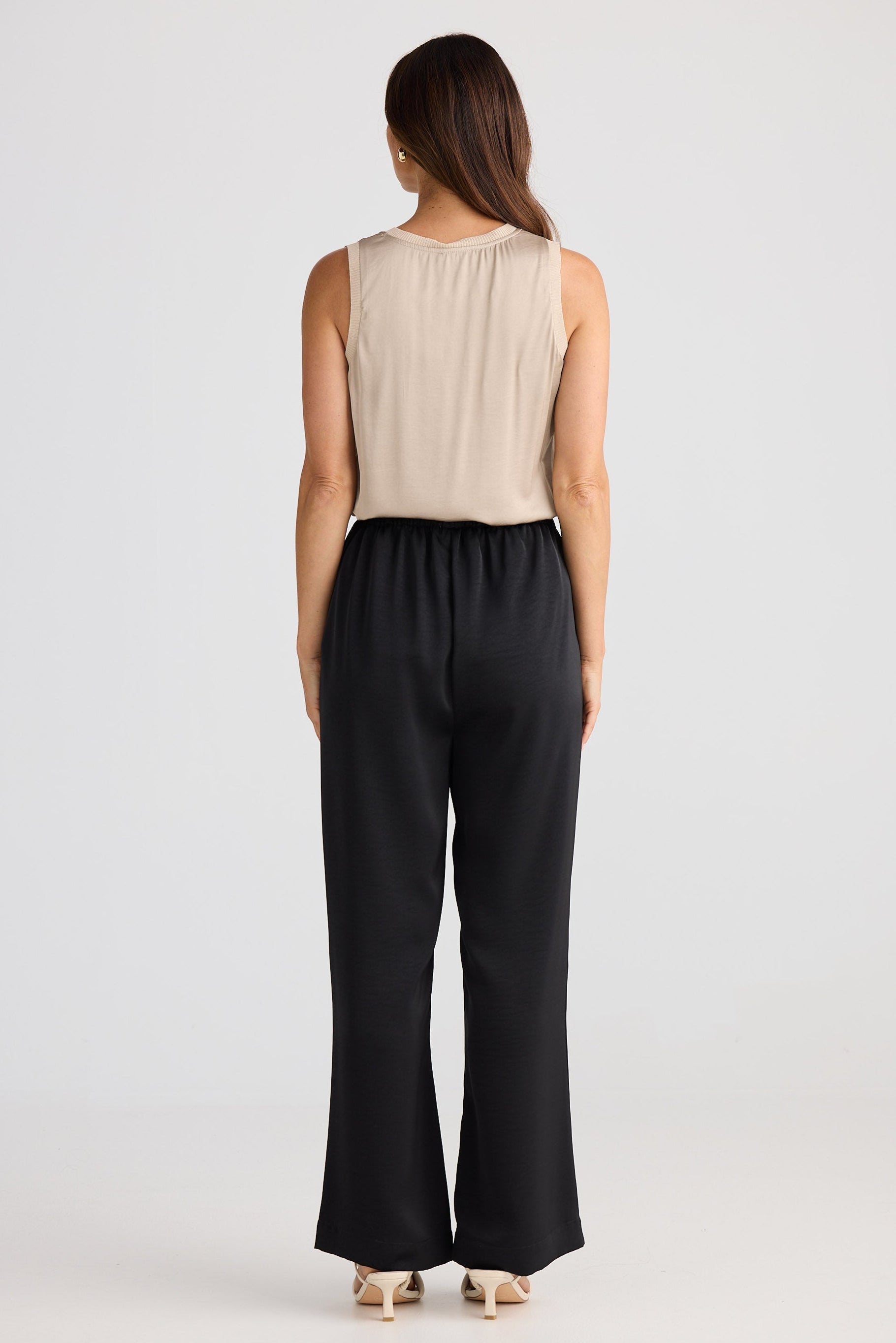 Woman wearing a beige sleeveless top and black high-waisted pants on a white background
