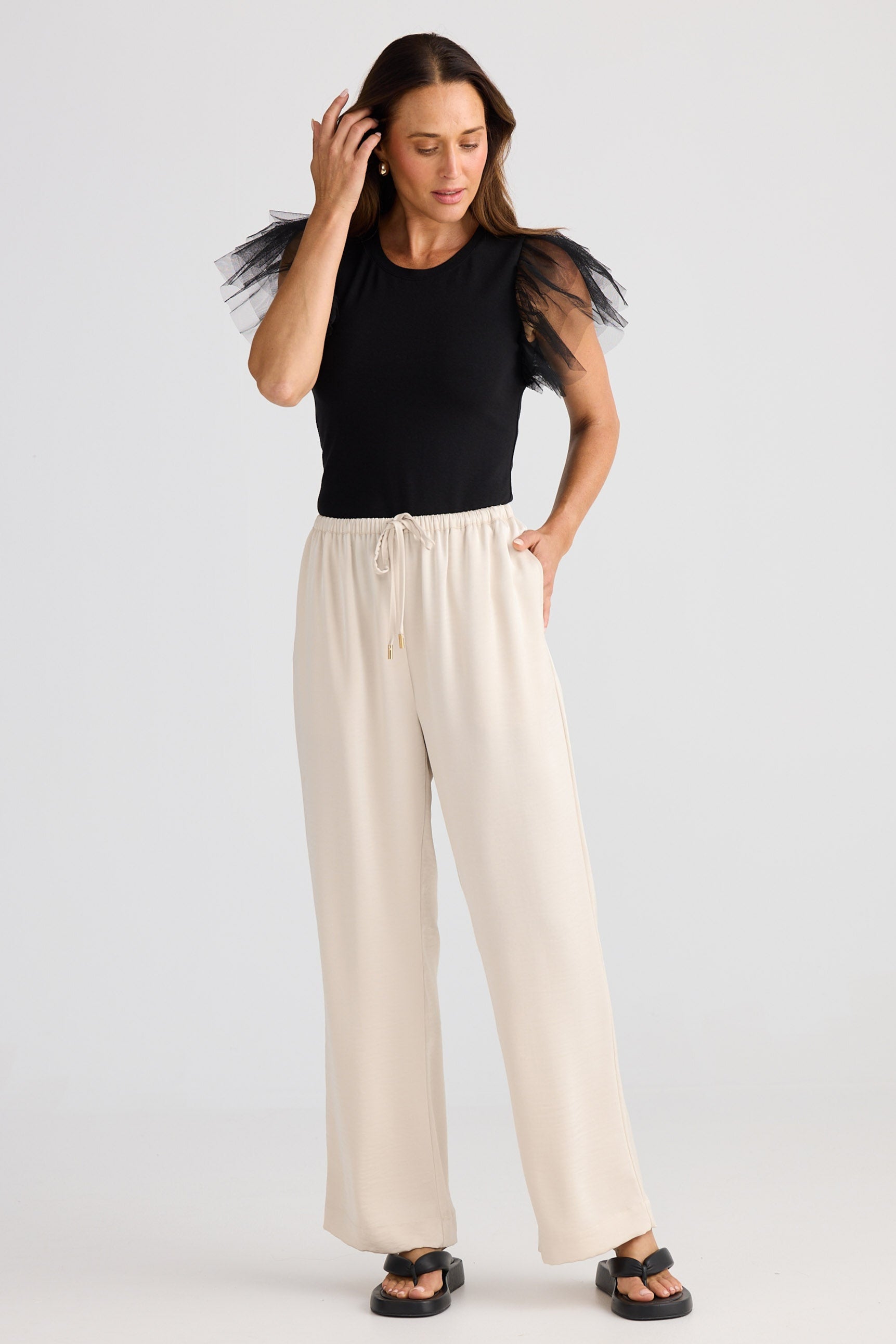 Woman wearing a black top and beige pants on a white background
