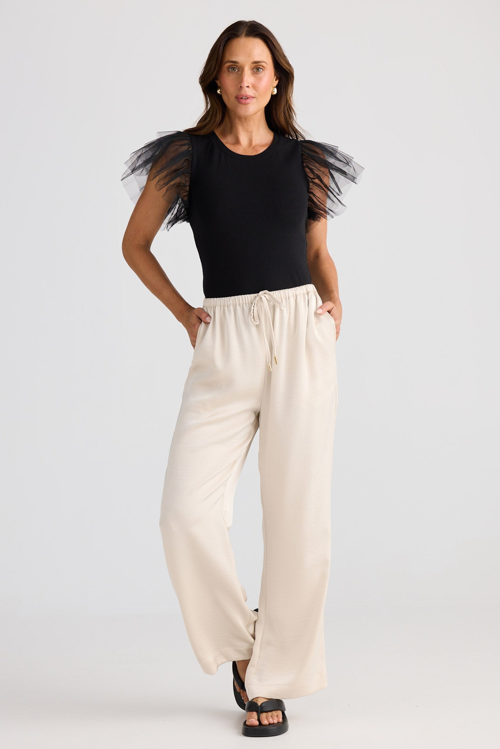 Woman wearing a black top with sheer sleeves and beige pants on a white background
