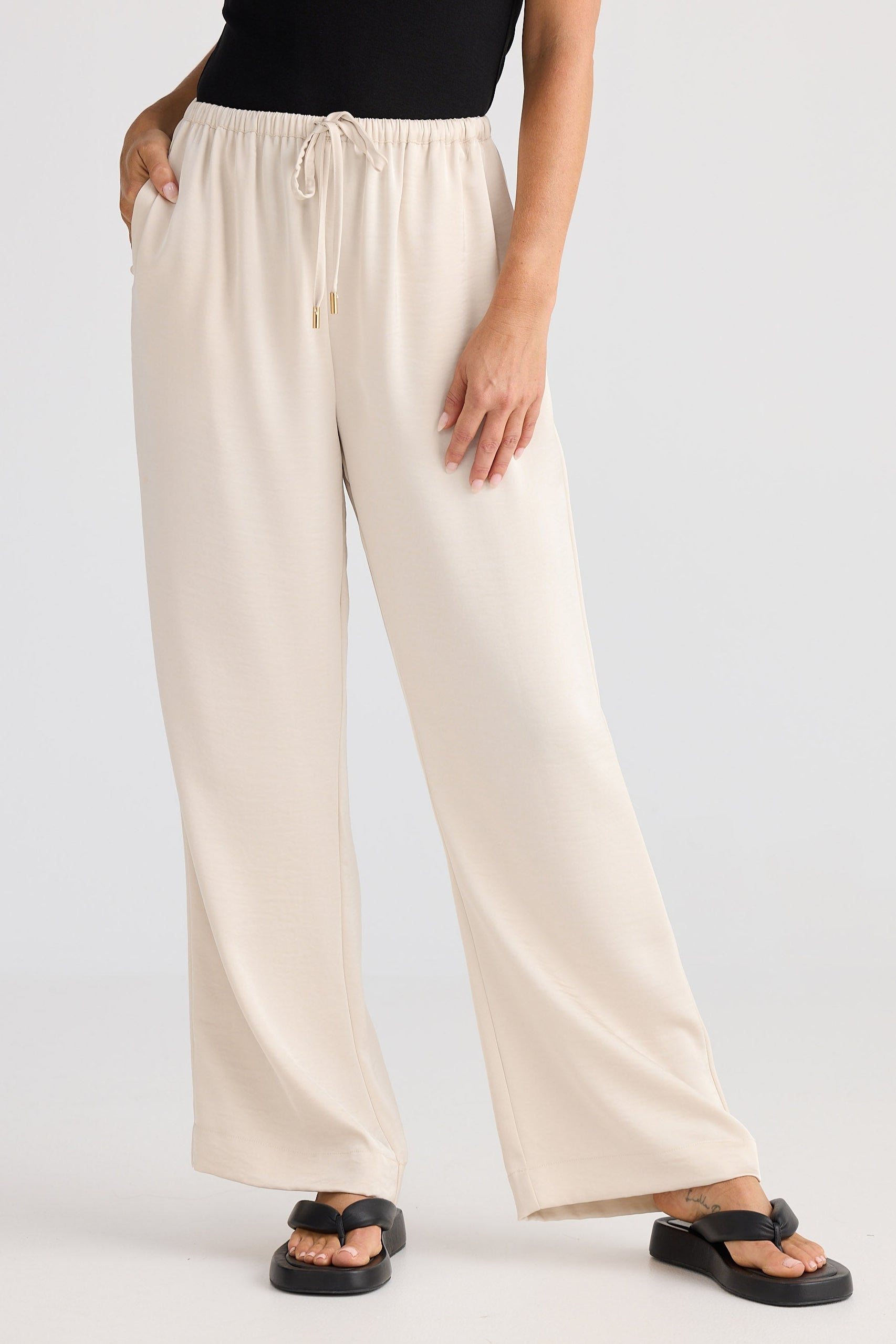 Person wearing beige wide-leg pants on a white background
