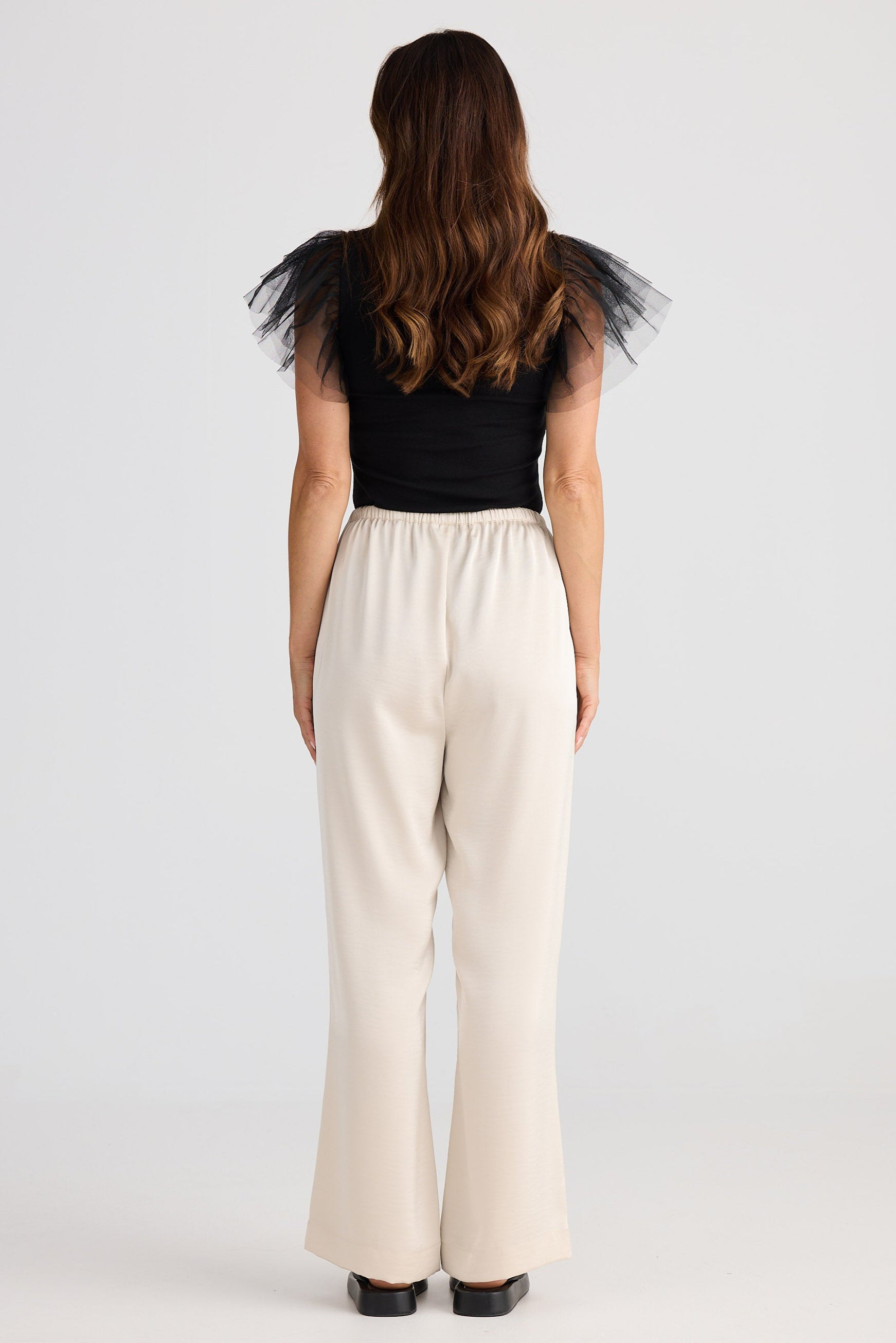 Person wearing a black sleeveless top with sheer sleeves and beige pants on a white background