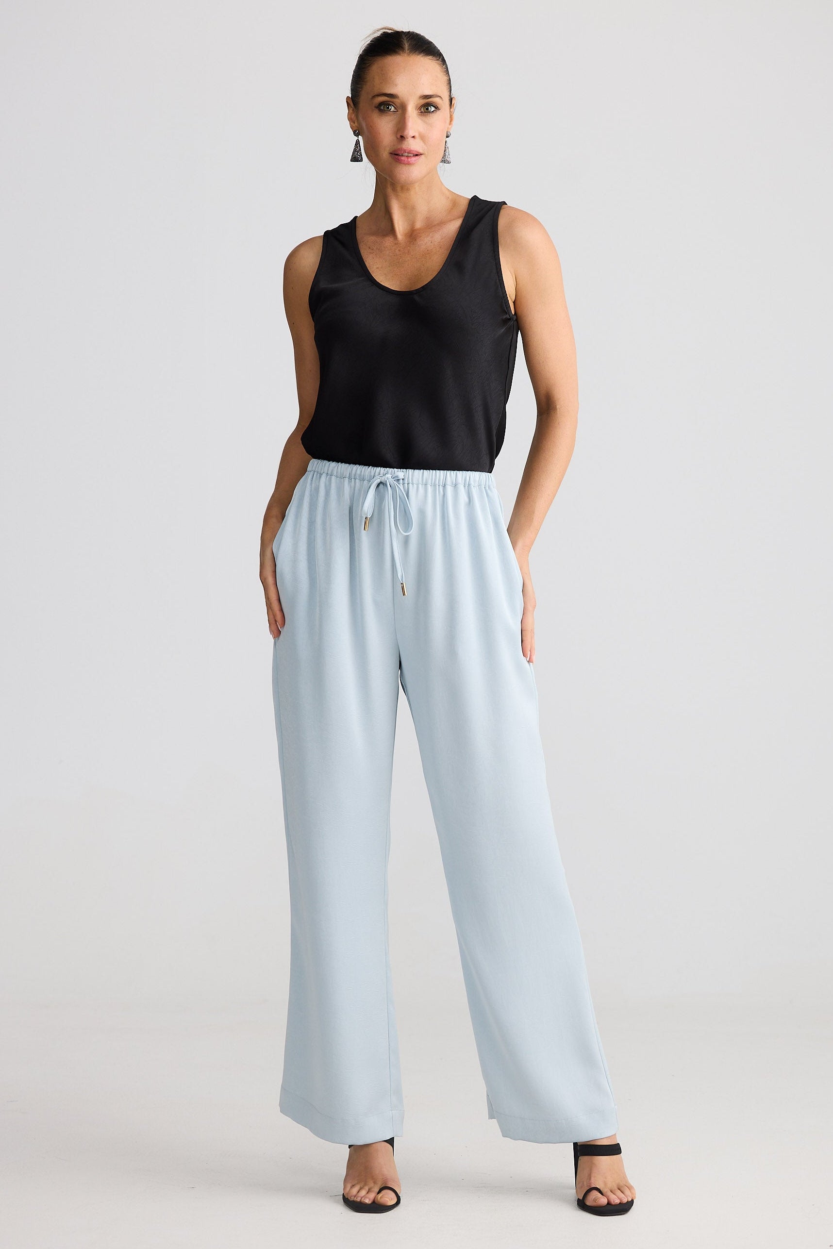 Woman wearing a black sleeveless top and light blue pants on a white background