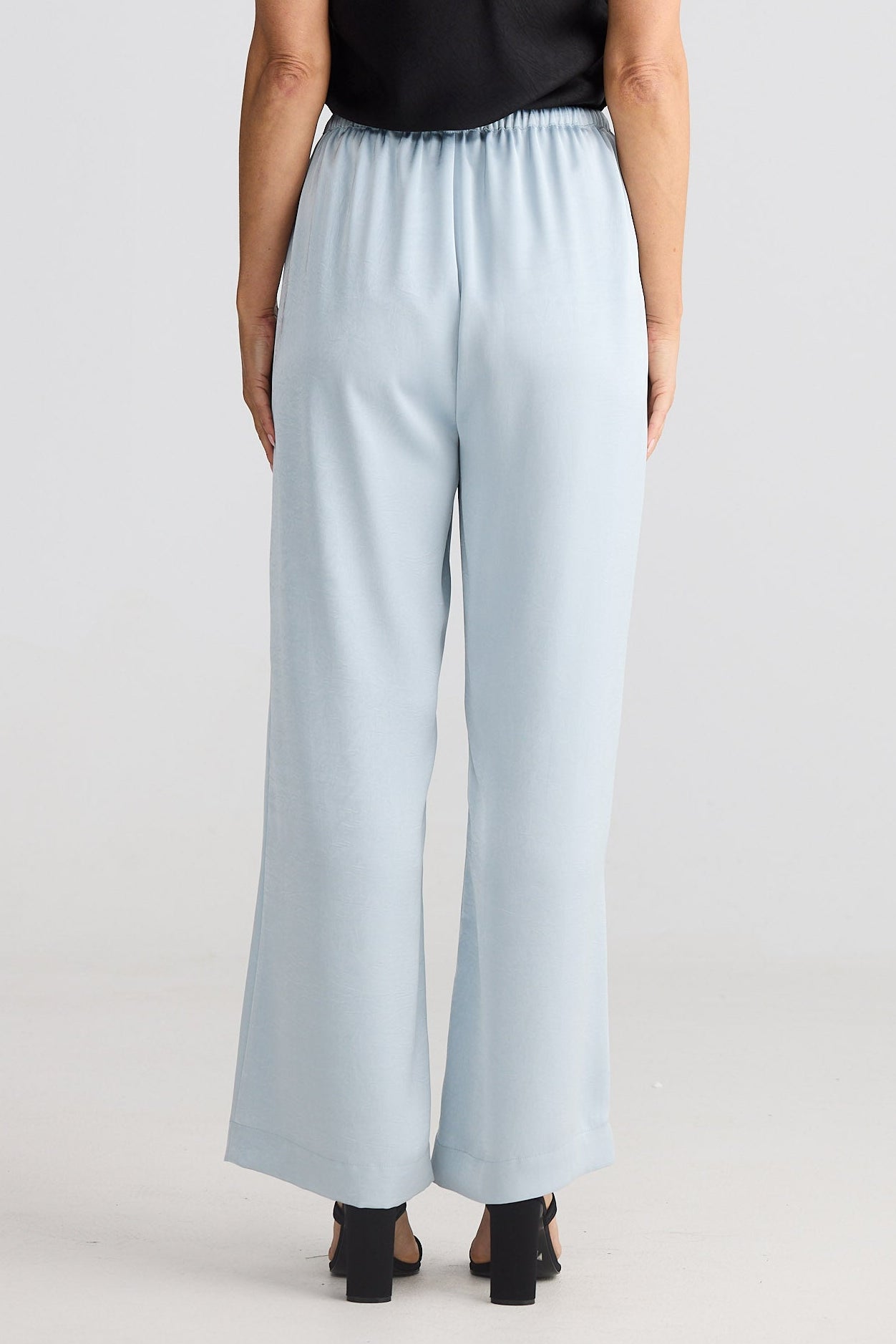 Person wearing a black sleeveless top and light blue pants on a white background