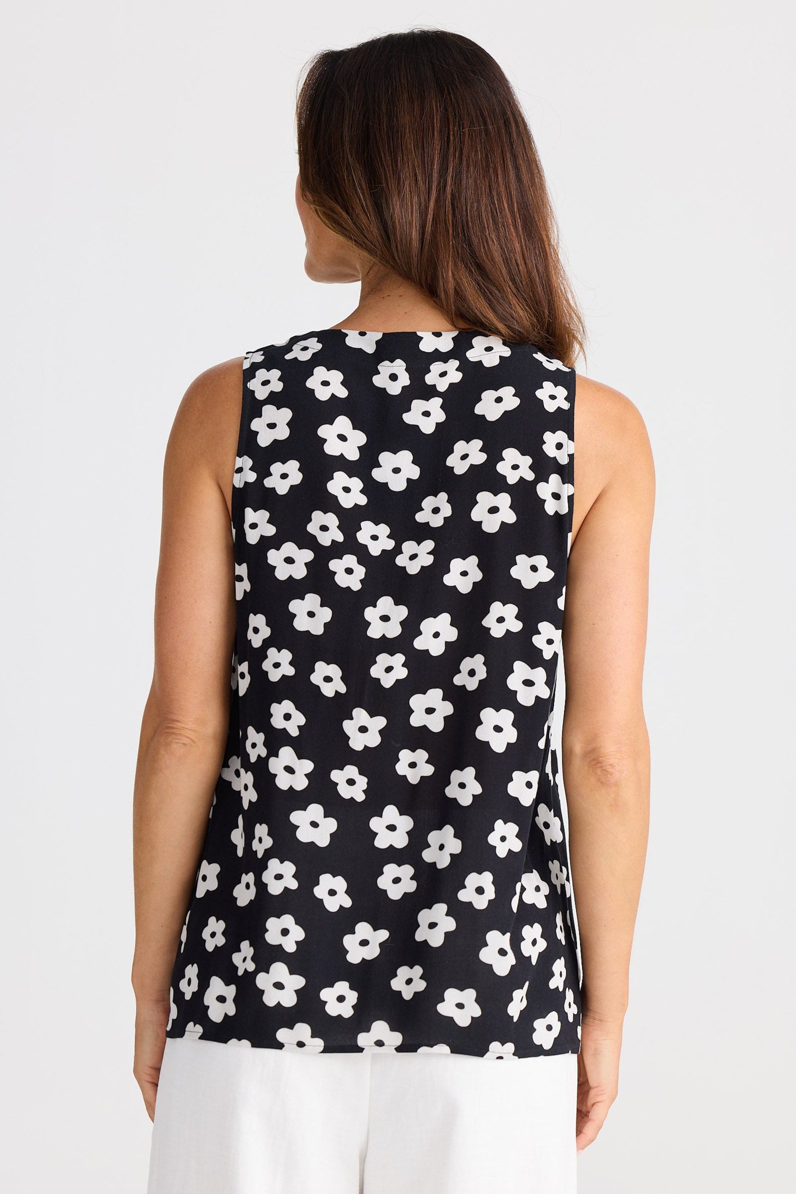 Woman wearing a sleeveless top with white floral pattern on a plain background