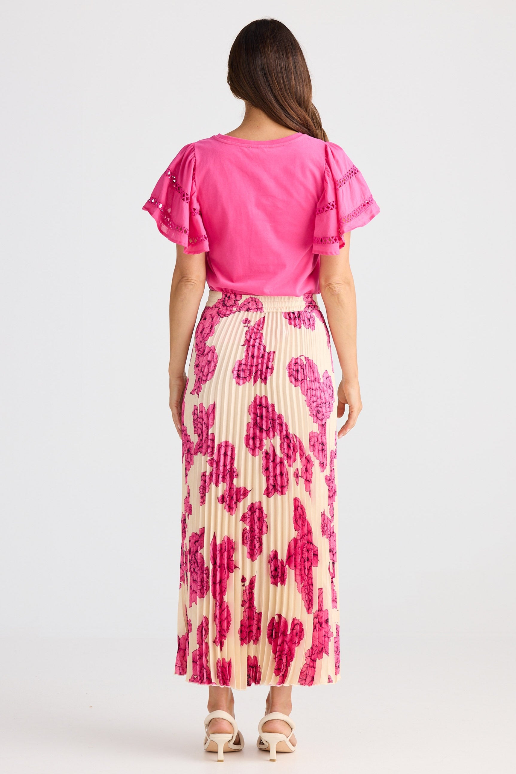 Woman wearing a pink top and patterned skirt on a white background