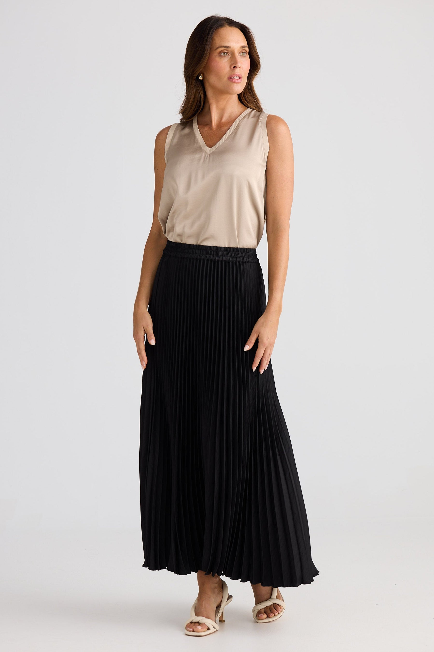 Woman wearing a beige sleeveless top and black pleated skirt on a white background